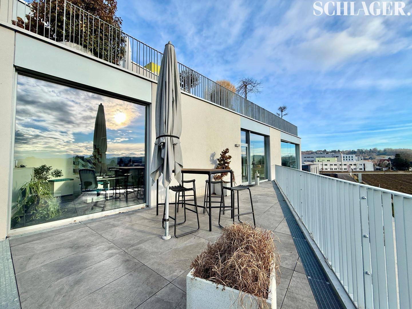 Große Dachterrasse mit Sonnenschirm, Stehtisch und weitem Blick über die Umgebung.