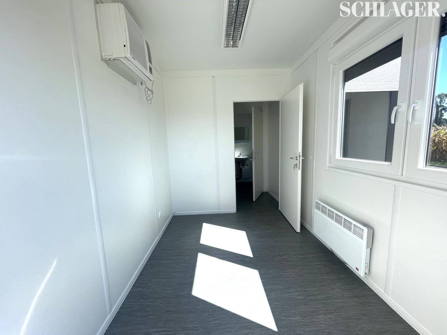 Kleines, helles Büro in einem Container mit Klimaanlage, Fenster und Heizkörper, ideal für temporäre Nutzung.