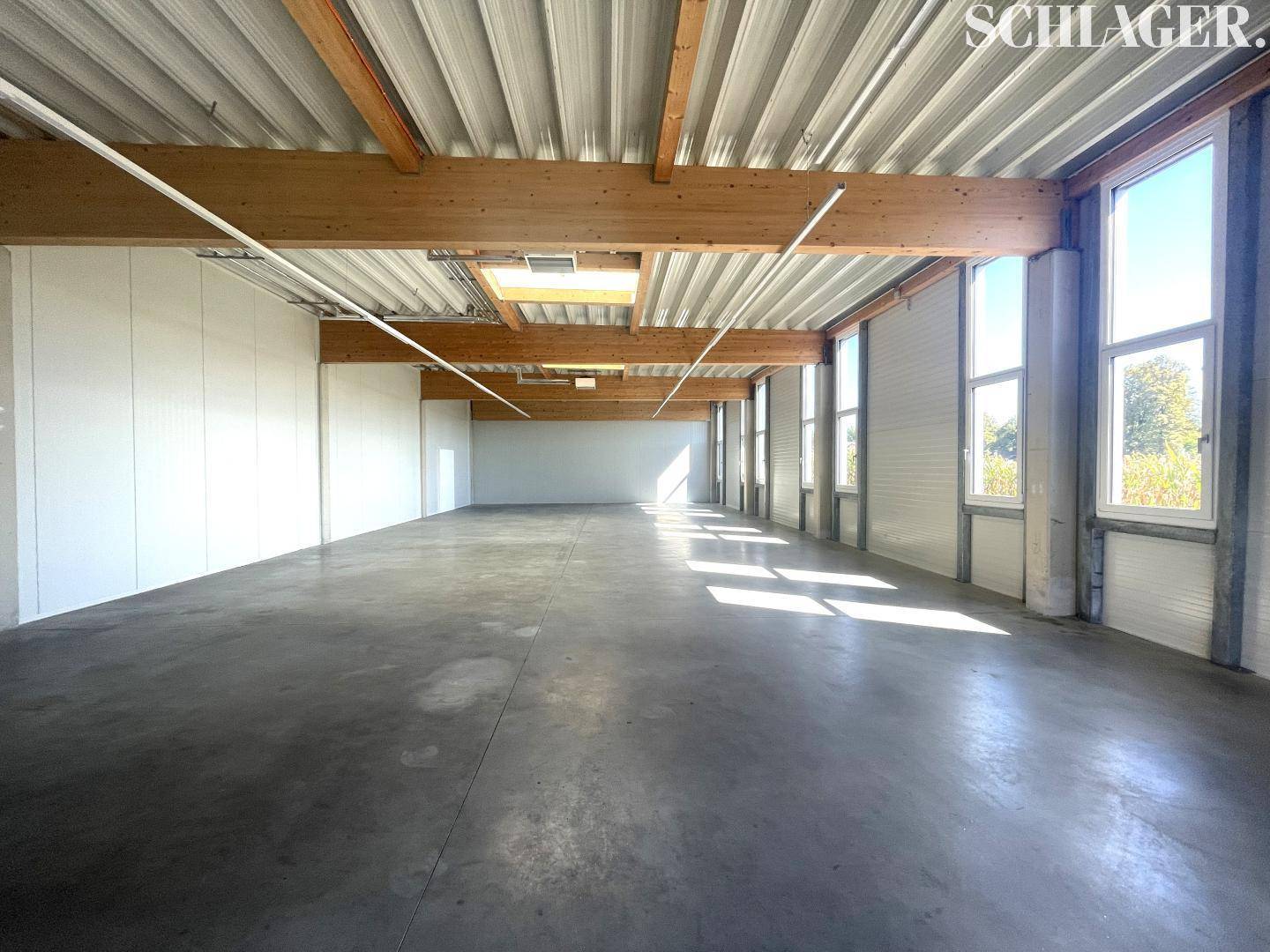 Geräumige Lagerhalle mit hohen Decken, sichtbaren Holzbalken und Betonboden, durchflutet von natürlichem Licht.
