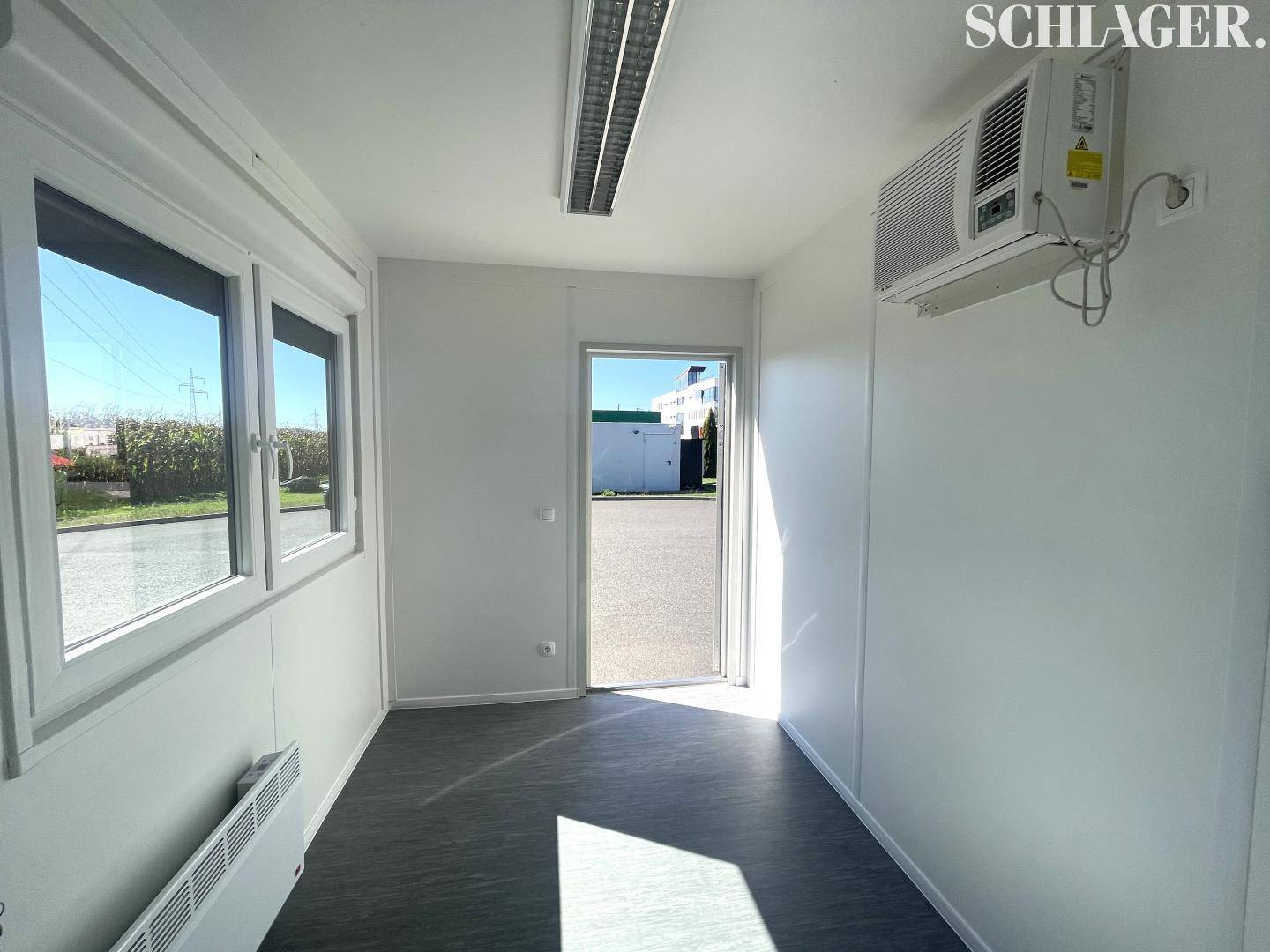 Modernes Containerbüro mit Klimaanlage, großen Fenstern und Blick auf den Außenbereich, gut beleuchtet.