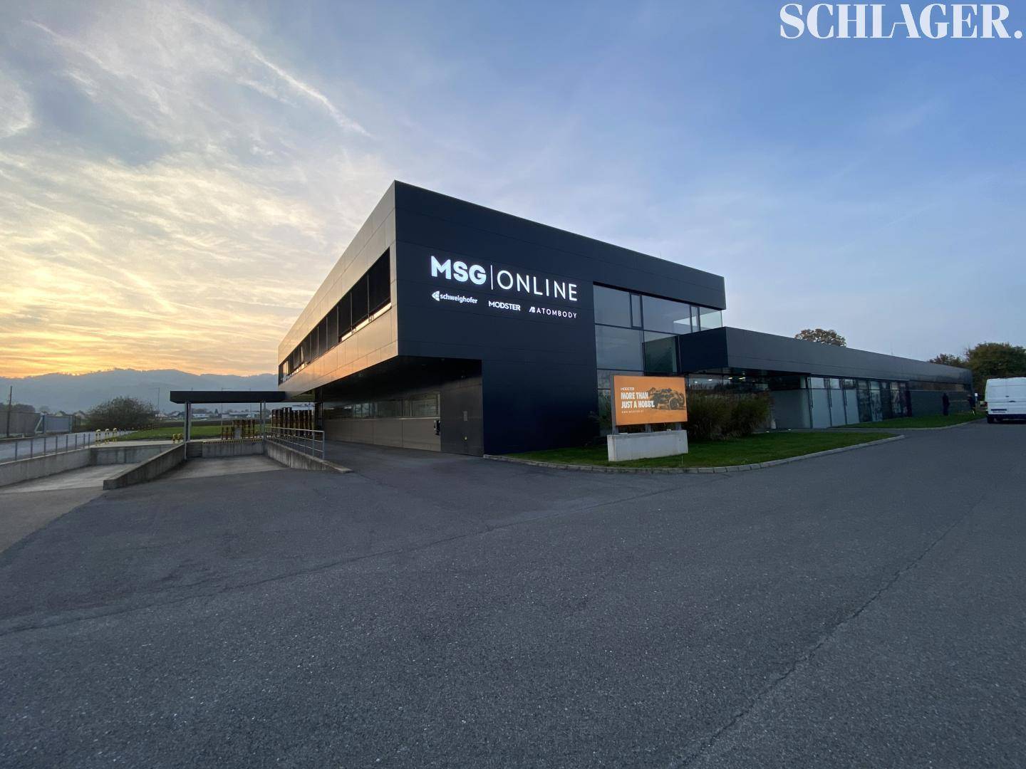 Das moderne Geschäftsgebäude bei Sonnenuntergang, mit beleuchtetem Firmenlogo und dunkler Fassade.