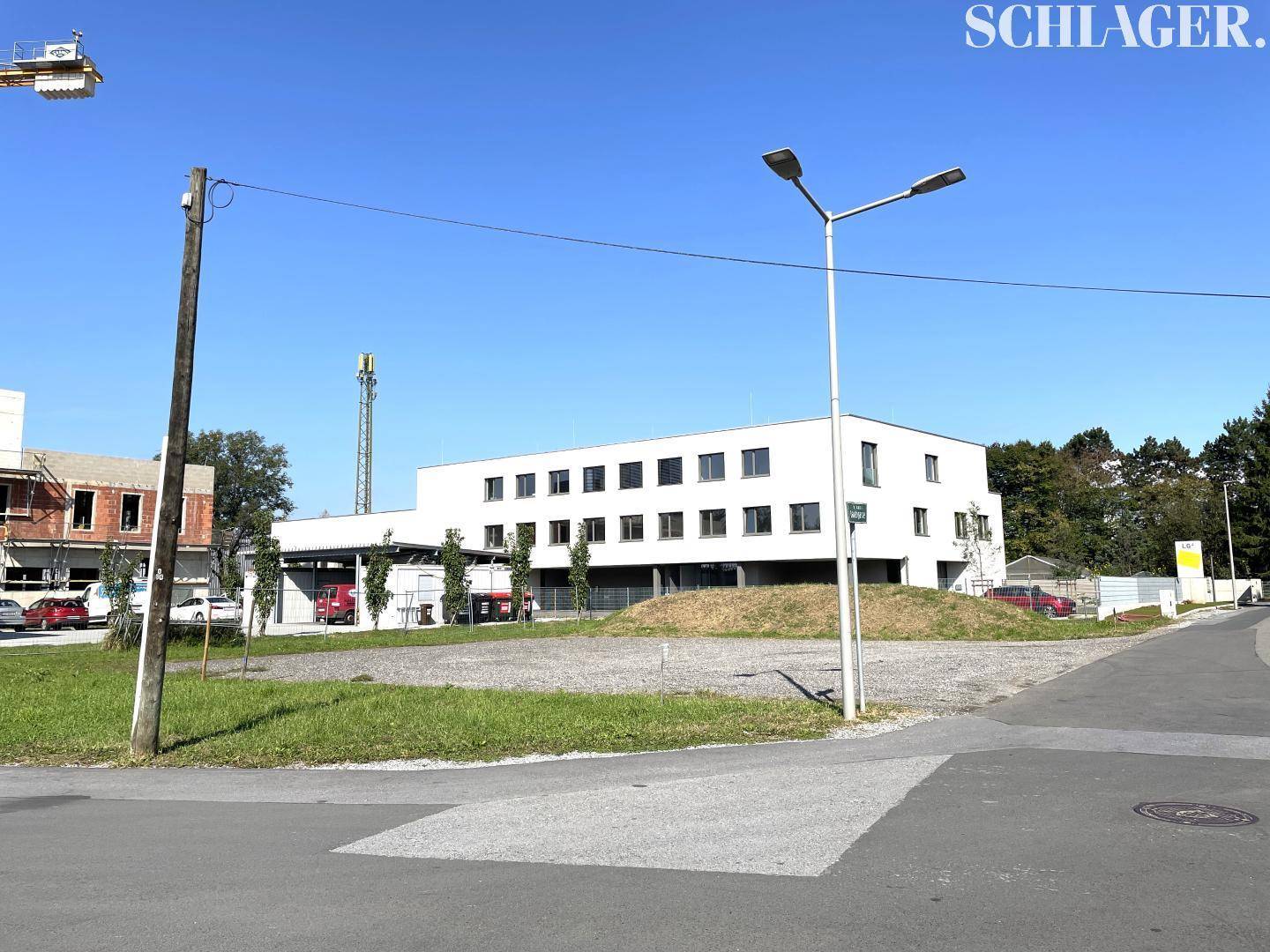 Unbebautes Grundstück neben einer Straße mit Laterne und einem modernen Gebäude im Hintergrund.