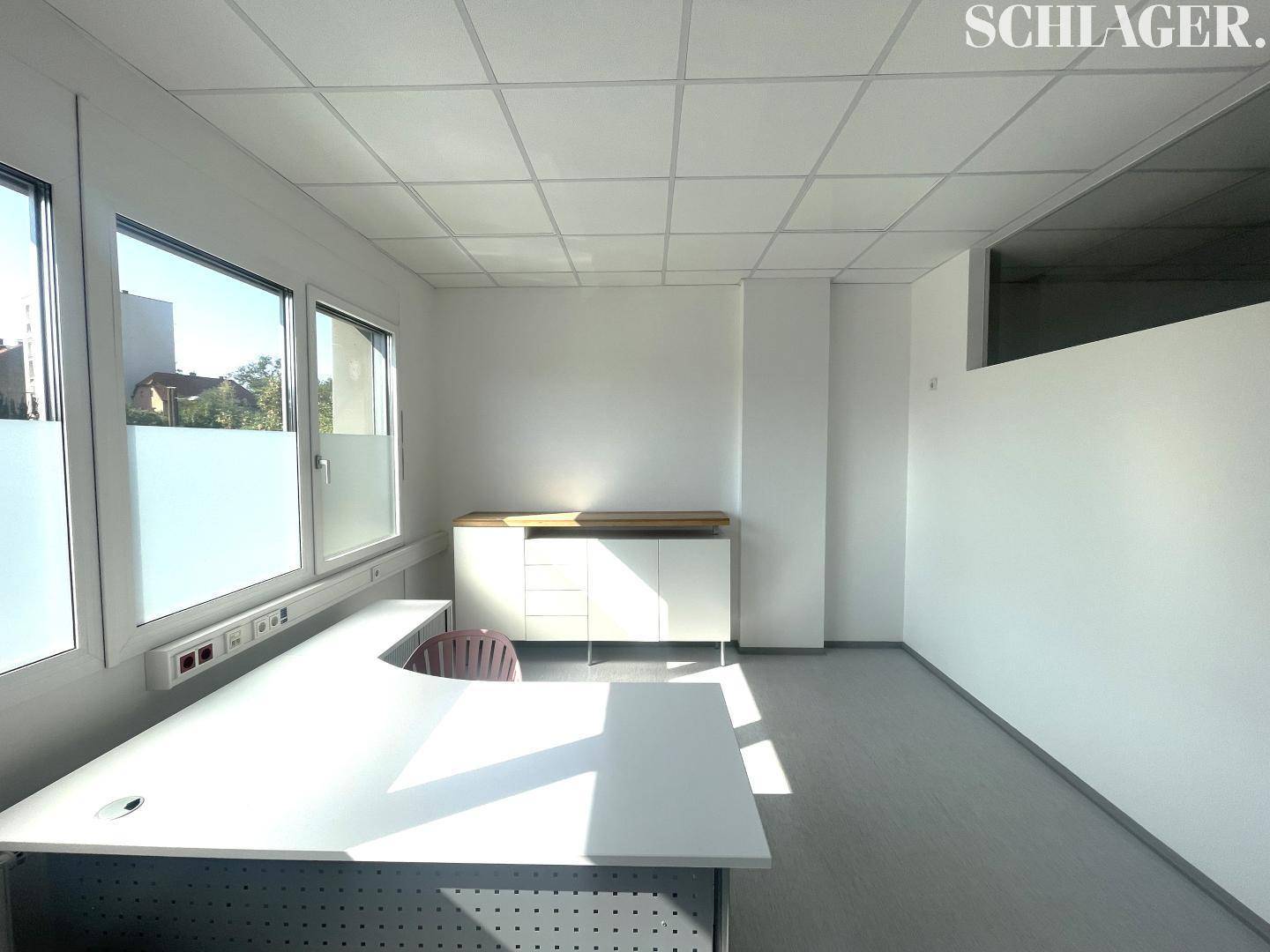Geräumiges Büro mit viel Tageslicht, einem modernen Schreibtisch und einem weißen Sideboard.