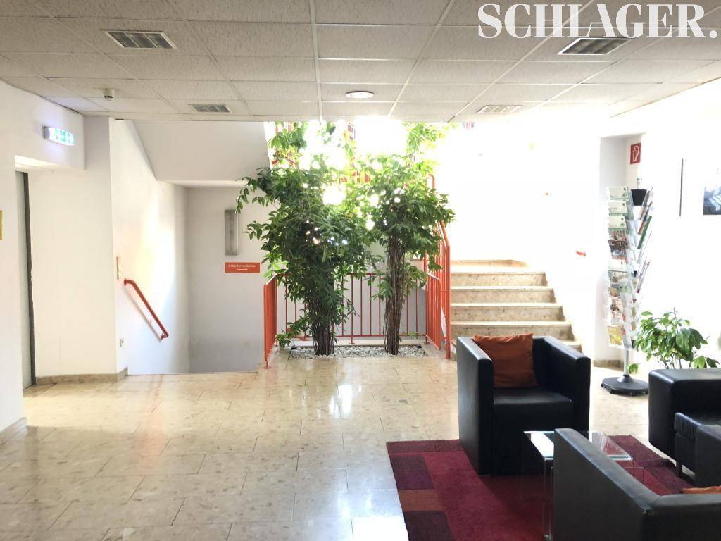 Empfangsbereich mit Treppe, Sitzgelegenheiten und dekorativen Pflanzen, hell und einladend gestaltet.