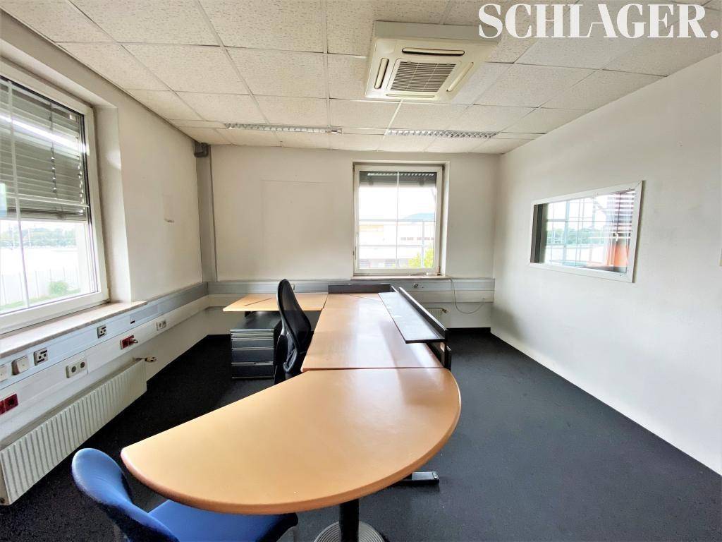 Büro mit einem geschwungenen Schreibtisch, Teppichboden und Fenstern, die viel Tageslicht hereinlassen.