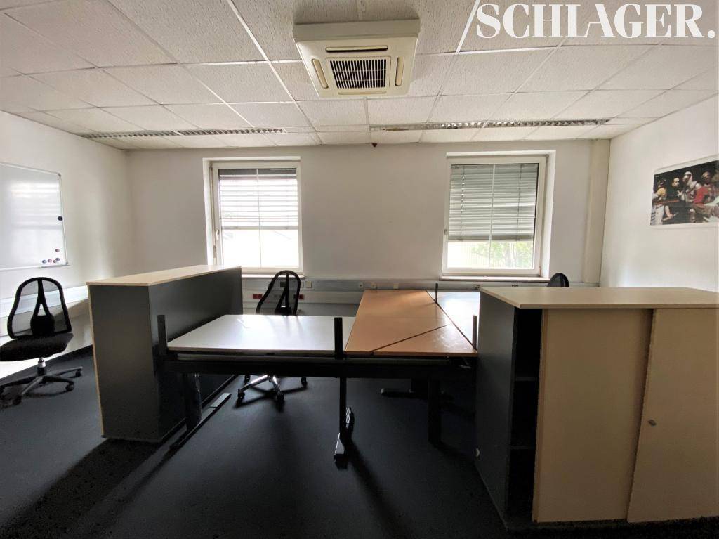 Großes Büro mit mehreren Arbeitsplätzen, einem Whiteboard und Fenstern für ausreichend Helligkeit.