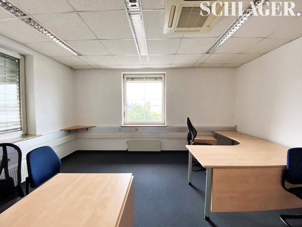 Helles Einzelbüro mit Teppichboden, einem Schreibtisch und einem Fenster für Tageslicht.