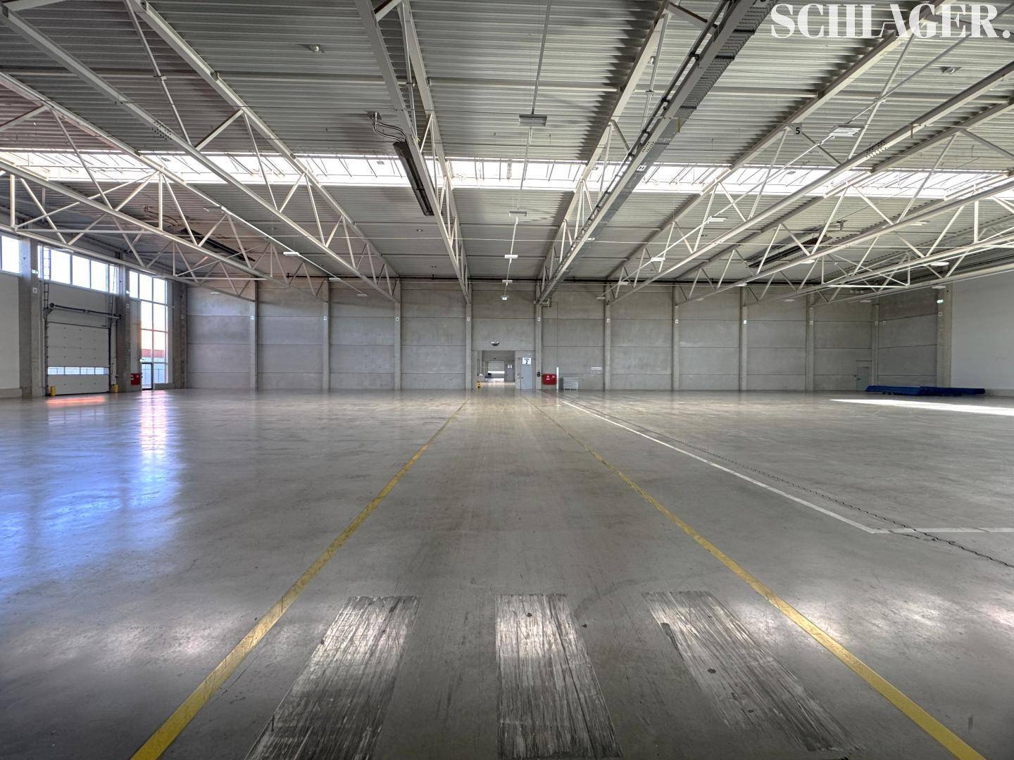 Weitläufige, leere Lagerhalle mit Betonboden und Markierungen, ideal für Logistik.