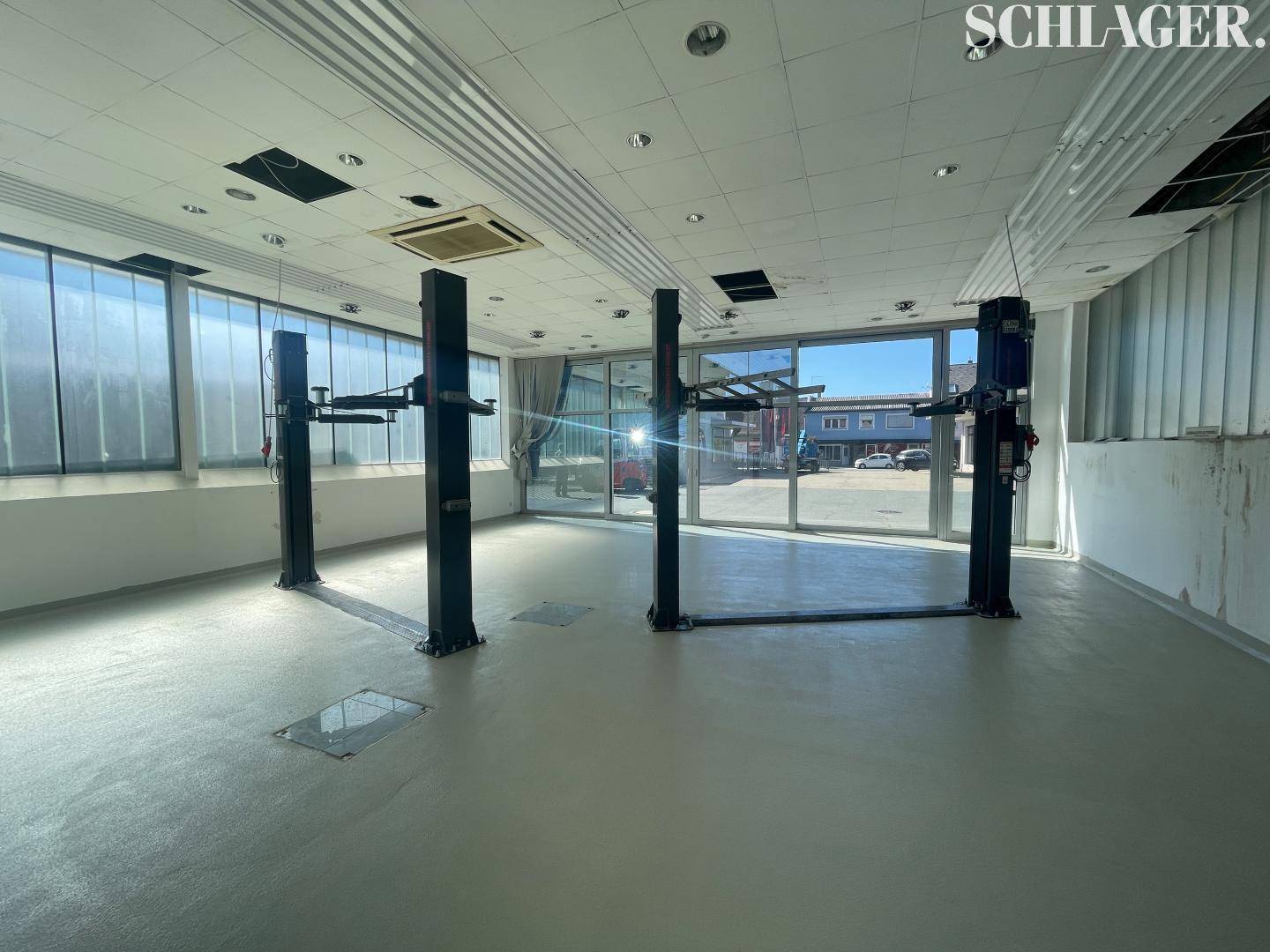 Heller Innenraum eines Servicebereichs mit zwei Hebebühnen und großen Fenstern zur Straße.