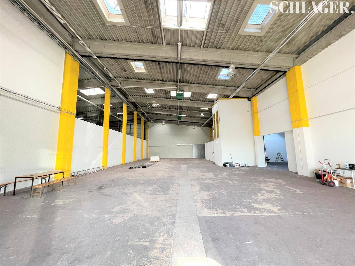 Geräumige, leere Industriehalle mit hohen Decken, Oberlichtern und Betonboden, bereit zur Nutzung.
