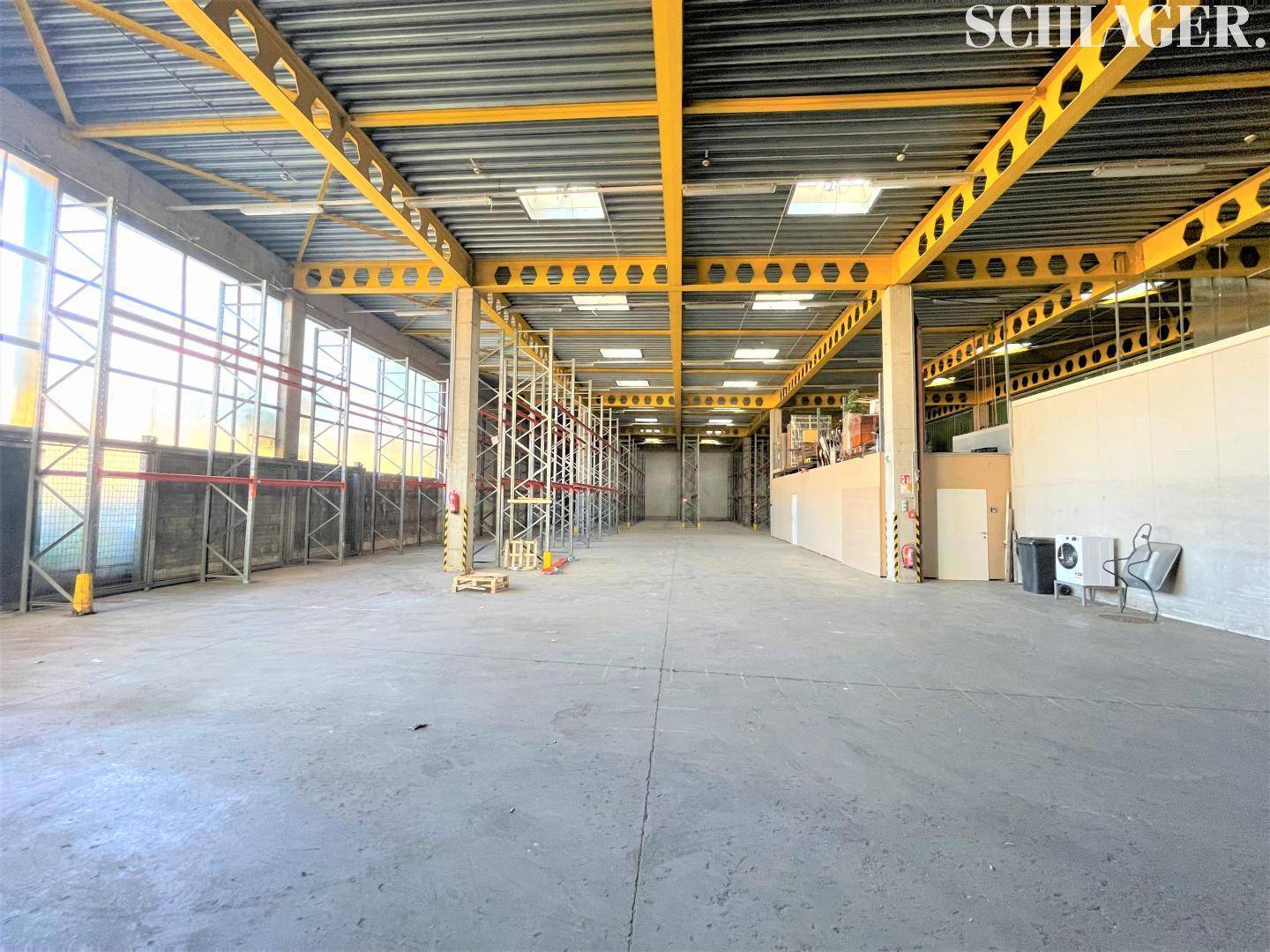 Große Lagerhalle mit hohen Decken, gelben Stahlträgern, Regalsystemen und einem robusten Betonboden.
