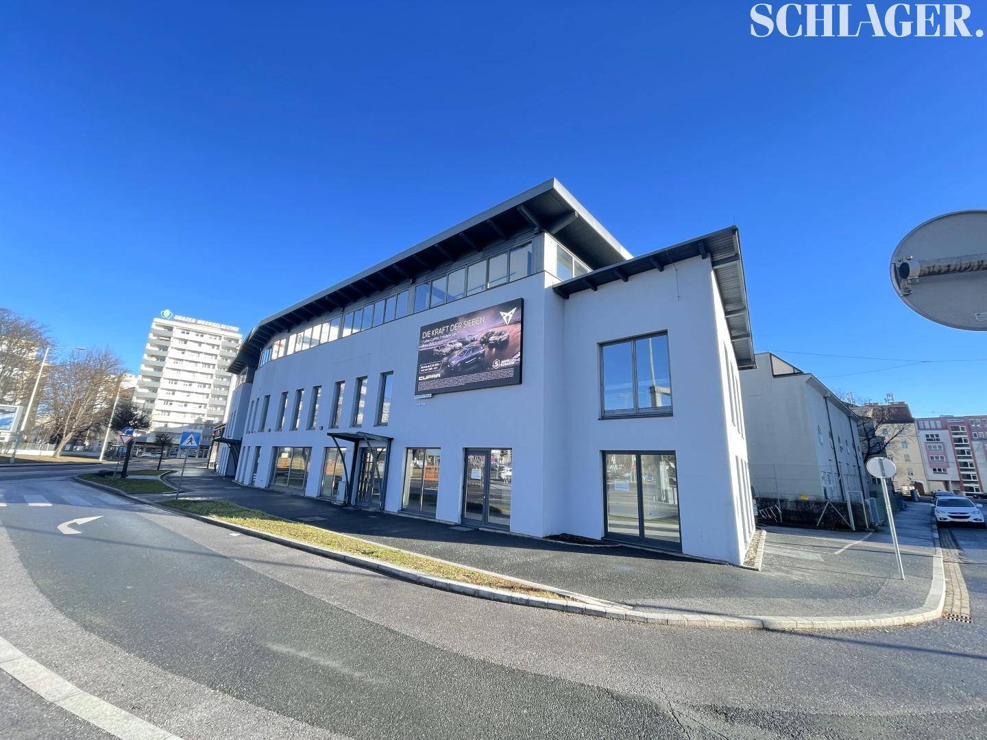 Seitenansicht eines modernen Geschäftsgebäudes mit großen Fenstern und einer Werbetafel an der Fassade an einem sonnigen Tag.