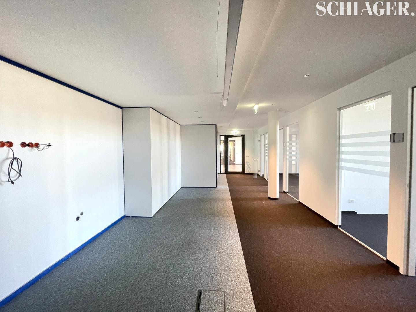 Langer Flur in einem Bürogebäude mit Teppichboden und mehreren Türen zu Büroräumen.