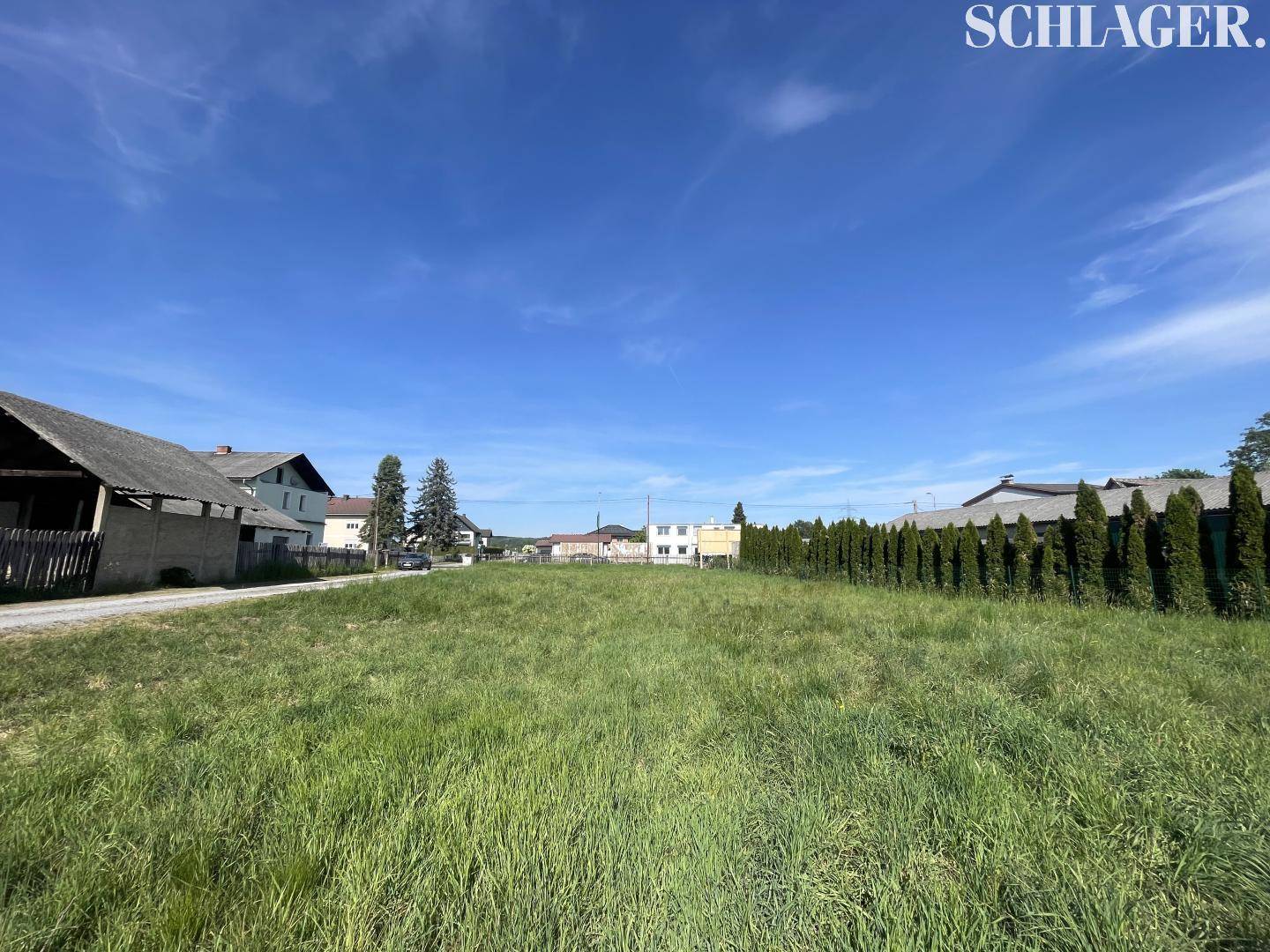 Weitläufiges, sonniges Grundstück mit grüner Wiese und Hecke im Hintergrund.