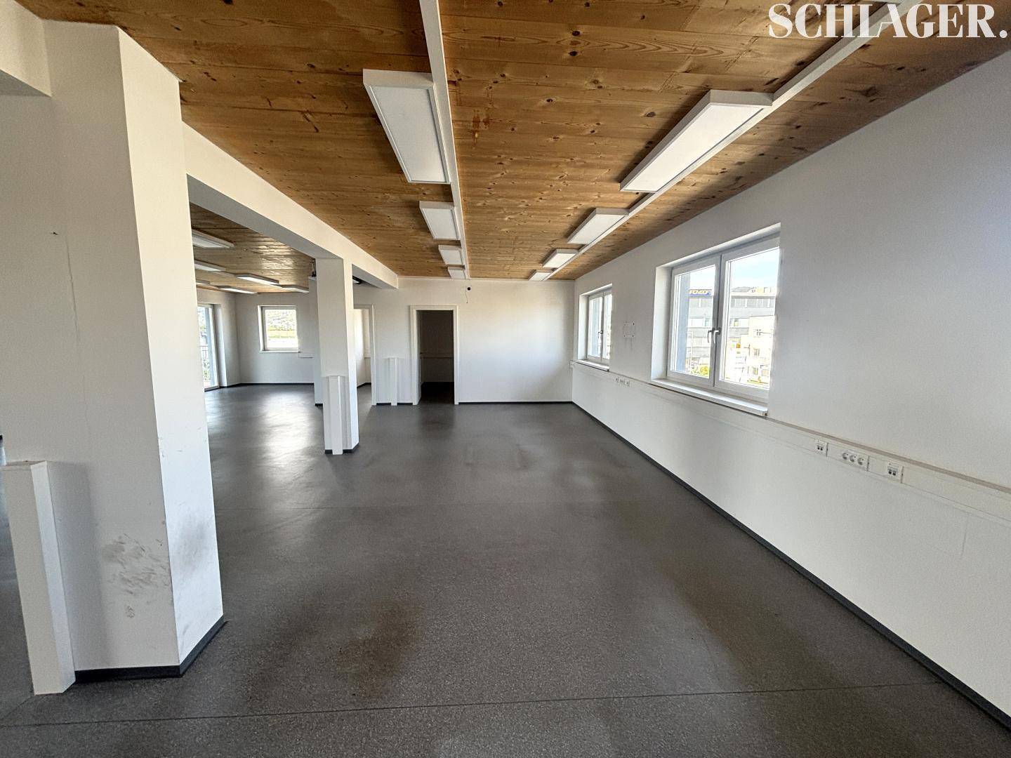 Großer, offener Bürobereich mit vielen Fenstern, Holzbalkendecke und modernem Betonboden.