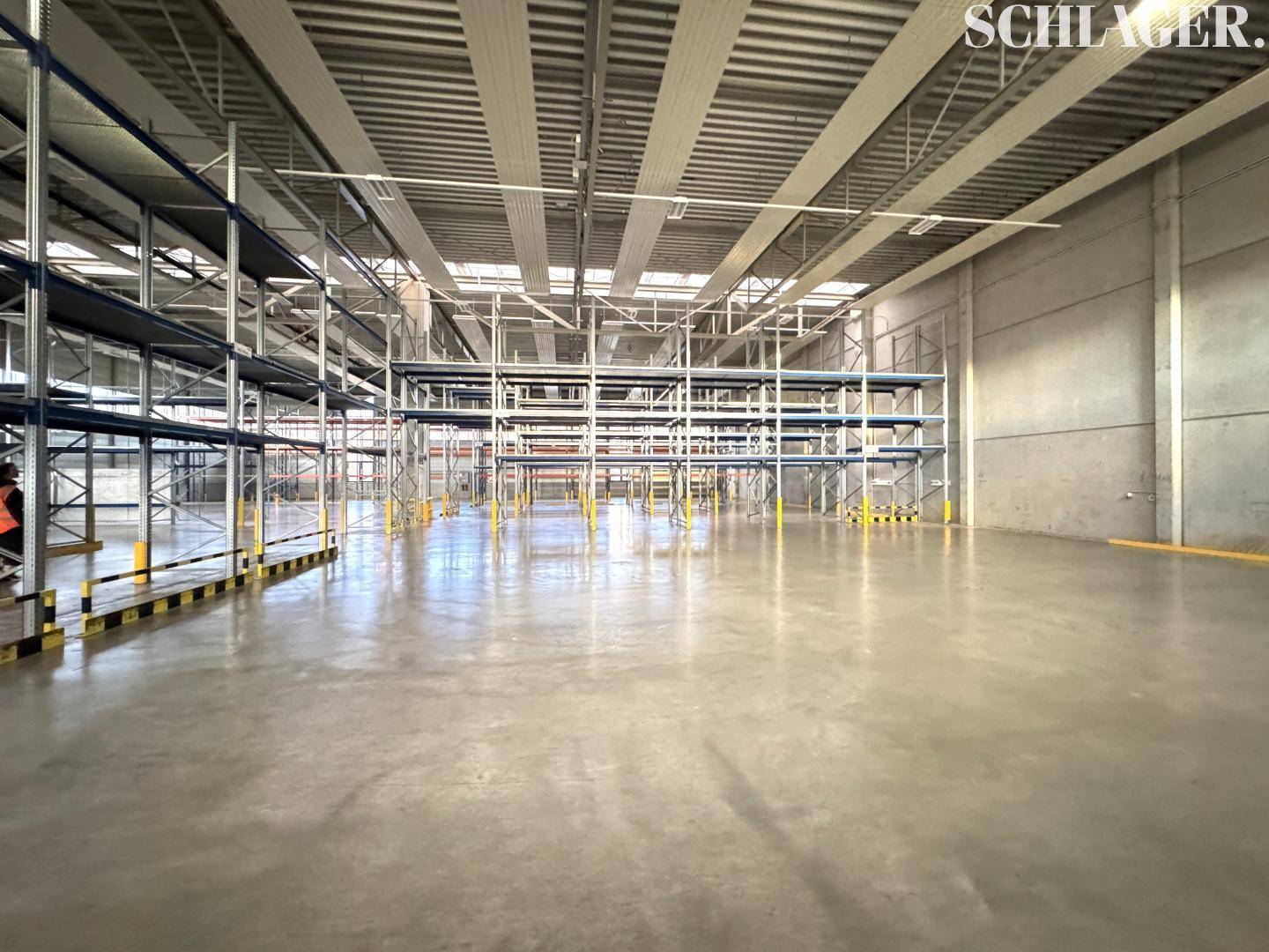 Weitläufige Lagerhalle mit umfangreichen Regalsystemen und natürlicher Belichtung durch Oberlichter.