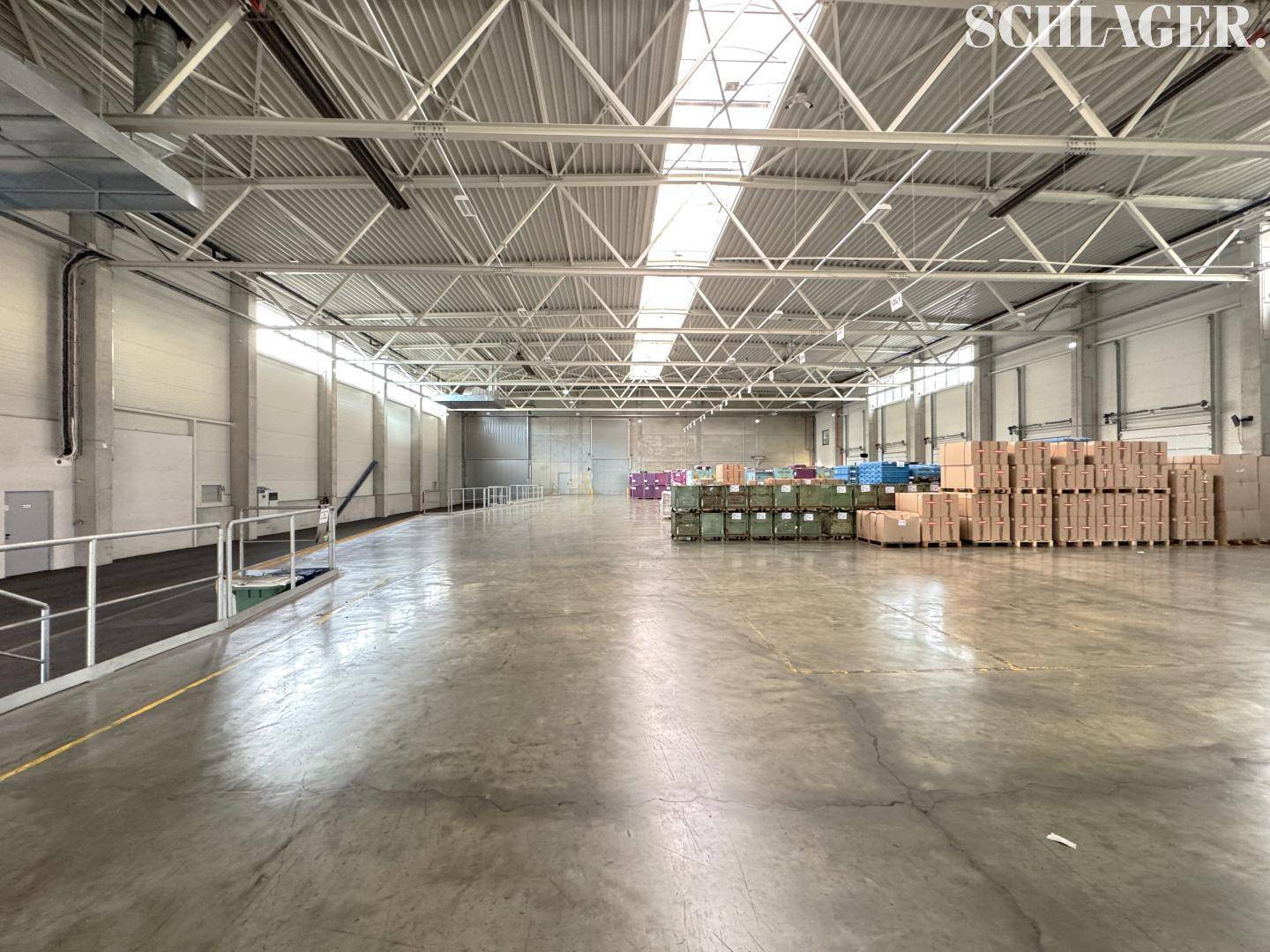 Weitläufige Industriehalle mit robustem Betonboden und heller Beleuchtung durch Dachfenster und Seitenfenster.