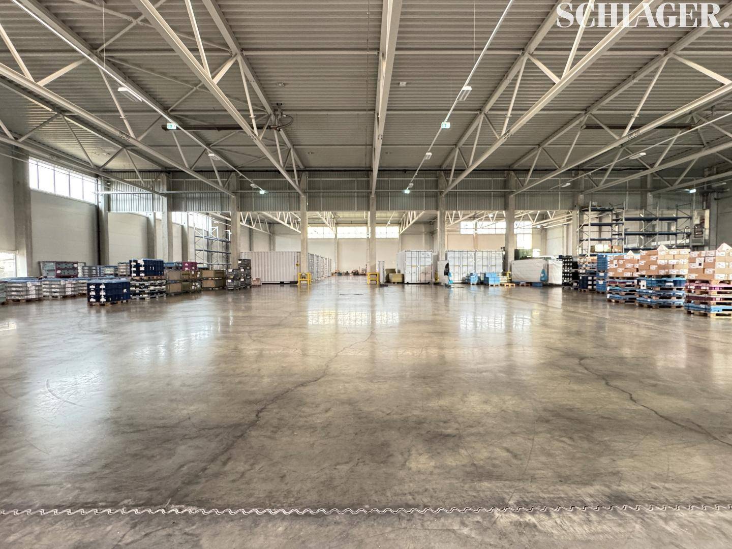 Helle und saubere Lagerhalle mit hoher Decke, Betonboden und Regalsystemen im Hintergrund für Warenlagerung.