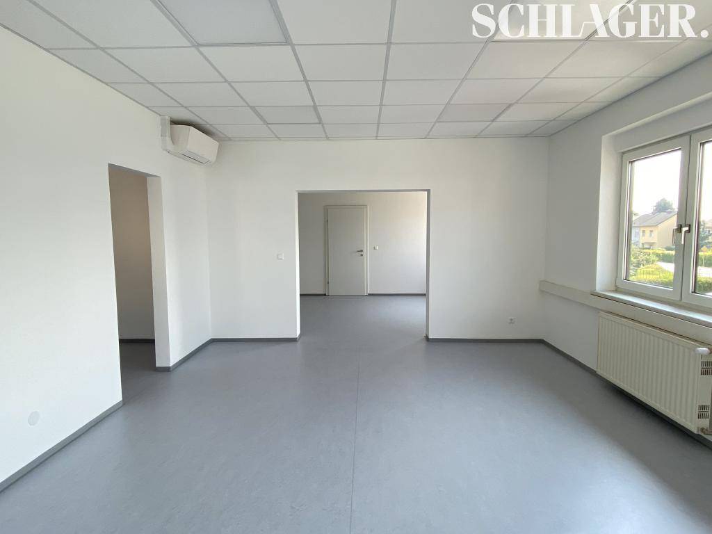 Leerer Bürobereich mit Zugang zu weiteren Räumen, Klimaanlage und hellen Wänden.