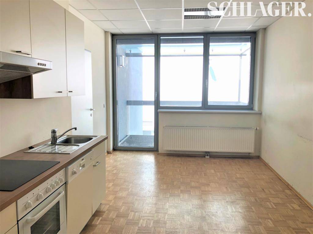 Kleine Einbauküche mit weißen Schränken, Herd und Spülmaschine, direktem Zugang zu einer Loggia.