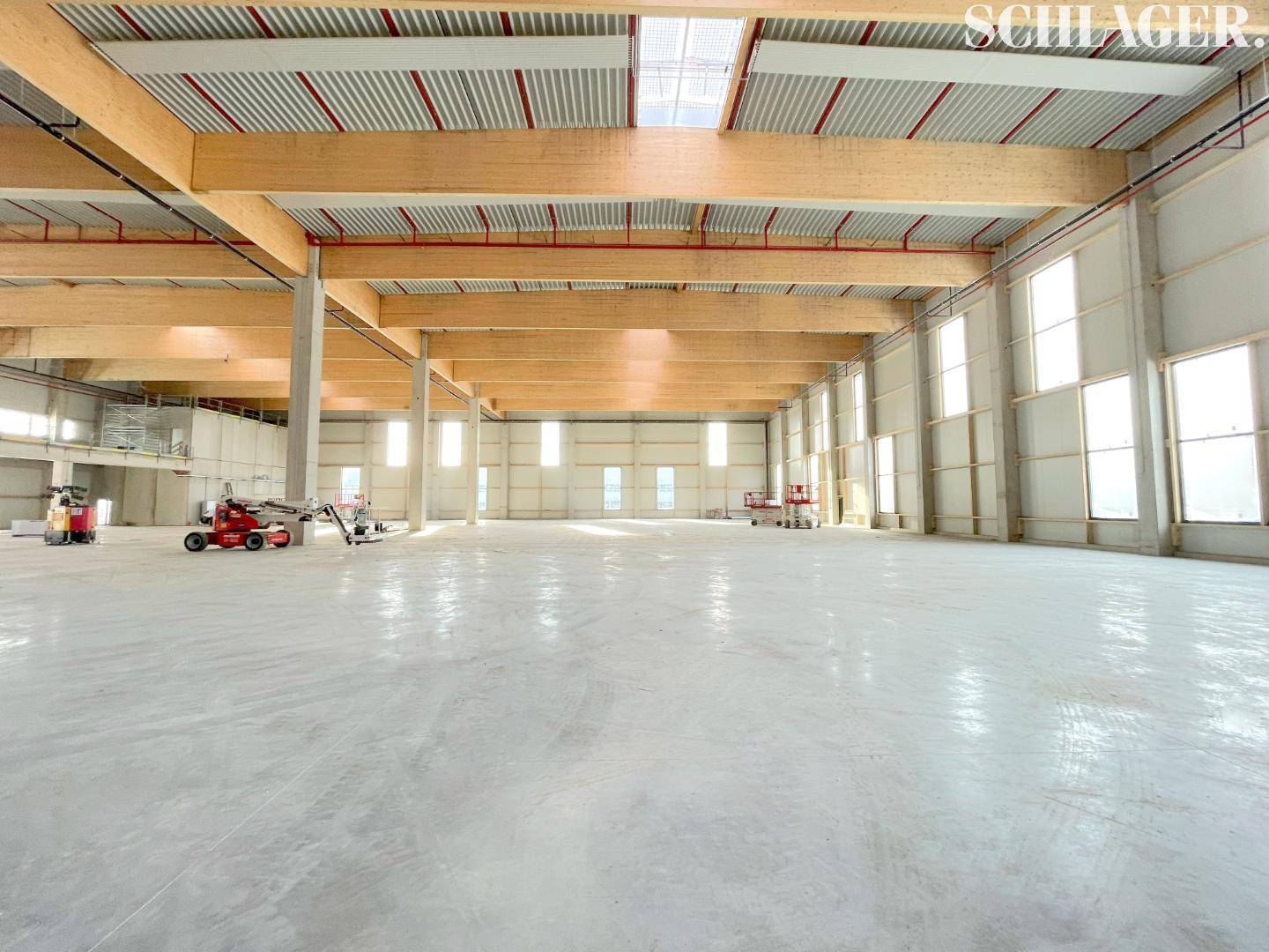 Geräumiger Lagerbereich mit hohen Decken, sichtbaren Holzbalken und viel Tageslicht durch zahlreiche Fenster.