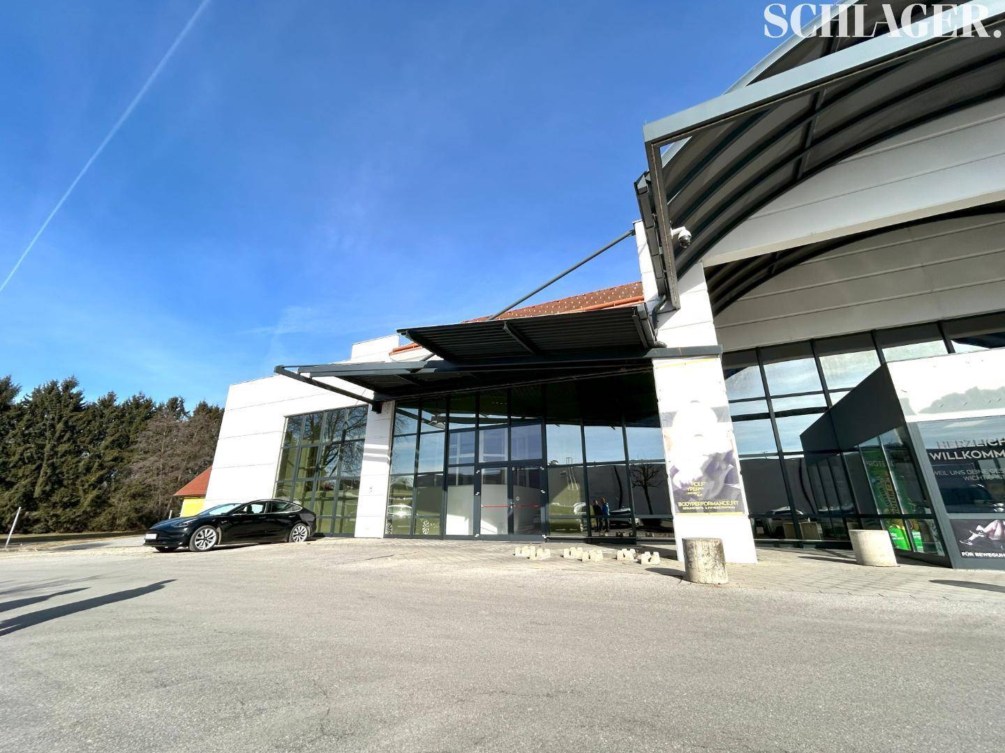 Eingangsbereich der modernen Gewerbeimmobilie mit großer Glasfront und Vordach an einem sonnigen Tag.