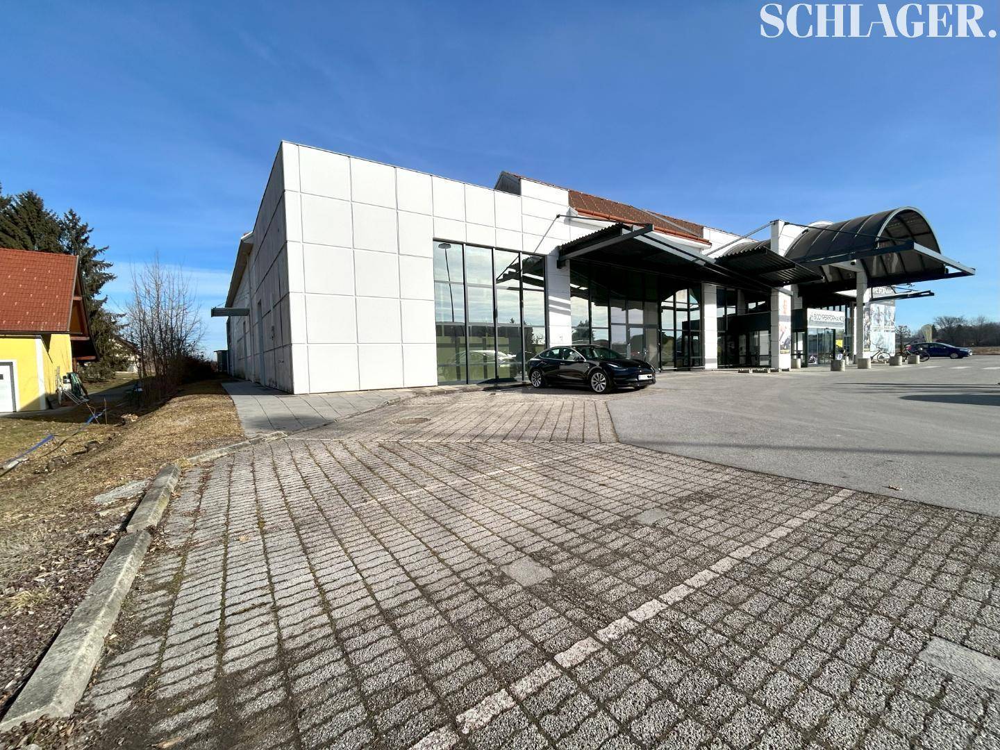Weitläufige Außenansicht der modernen Gewerbeimmobilie mit großem Parkplatz und gepflasterten Flächen.