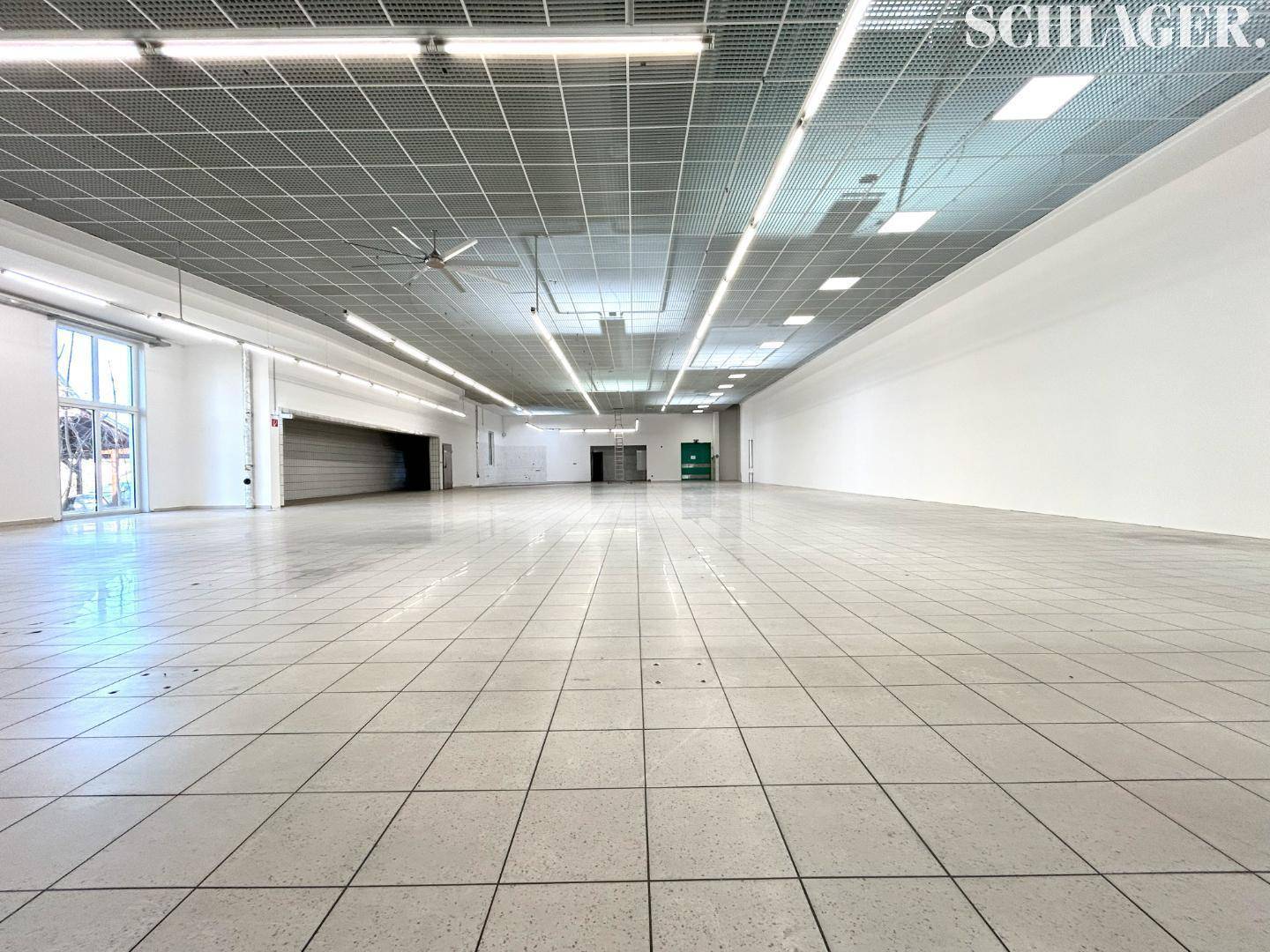 Weitläufiger Gewerberaum mit Fliesenboden, Rasterdecke und Rolltor im Hintergrund für Anlieferungen.
