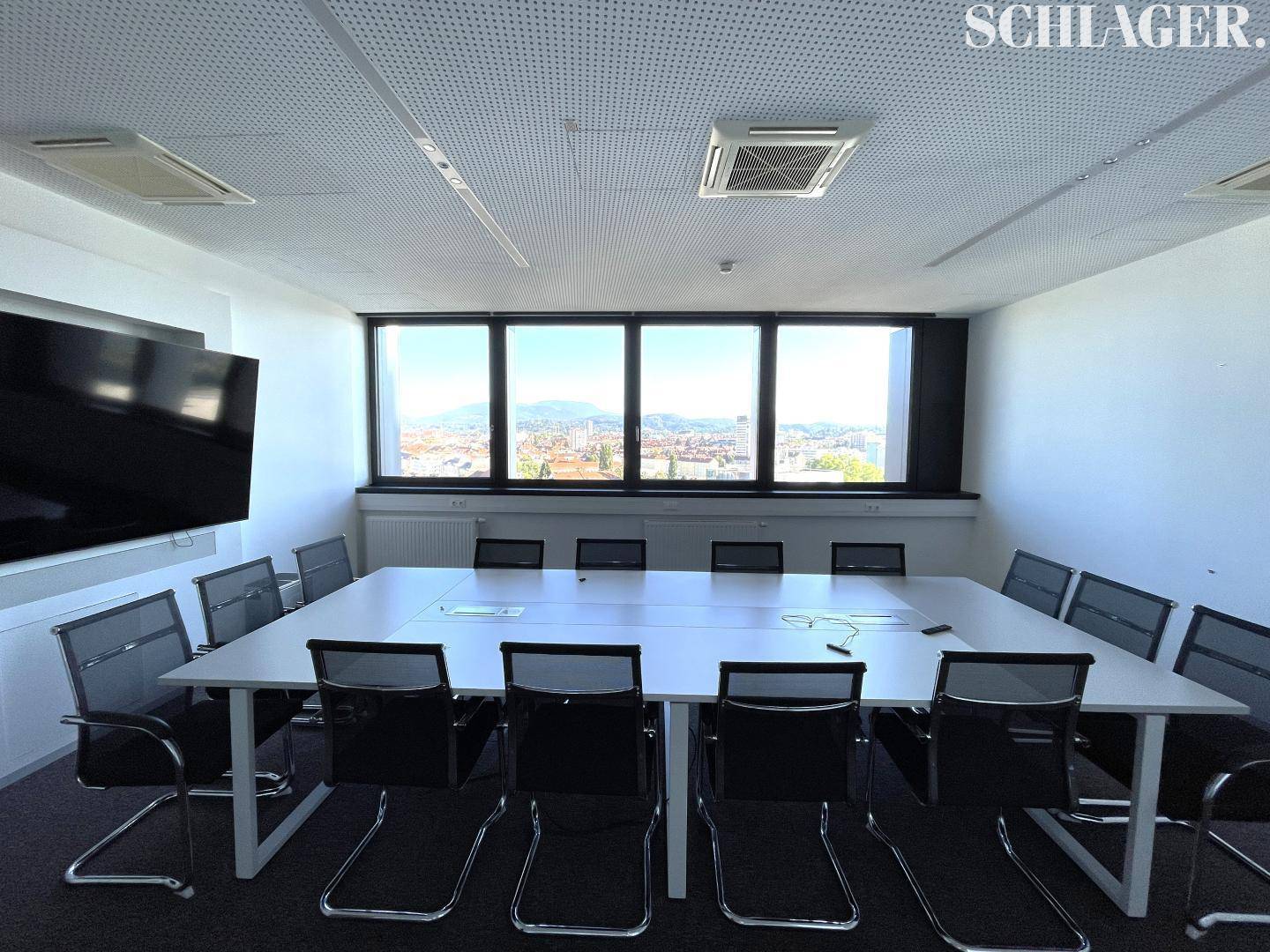 Großer Konferenzraum mit modernem Bildschirm, langem Tisch und Panoramablick auf die Stadt.