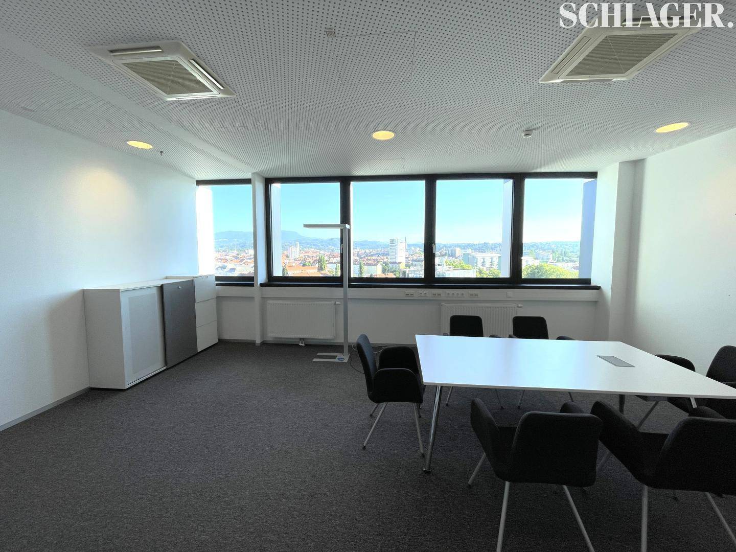 Heller Besprechungsraum mit weißem Tisch, grauen Stühlen und Blick auf die Stadt.
