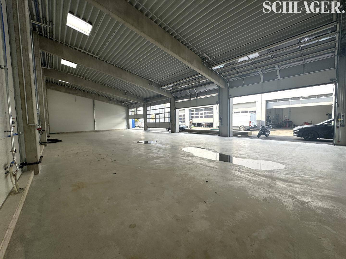 Weitläufiger Innenbereich einer modernen Lagerhalle mit Betonboden und Blick auf weitere Einheiten durch die Tore.