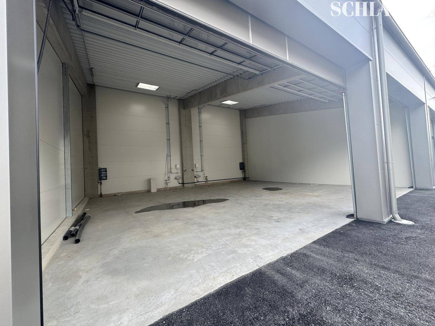 Geräumiger Innenraum einer Lagerhalle mit Betonboden, hohen Decken und großem Rolltor für den Zugang.