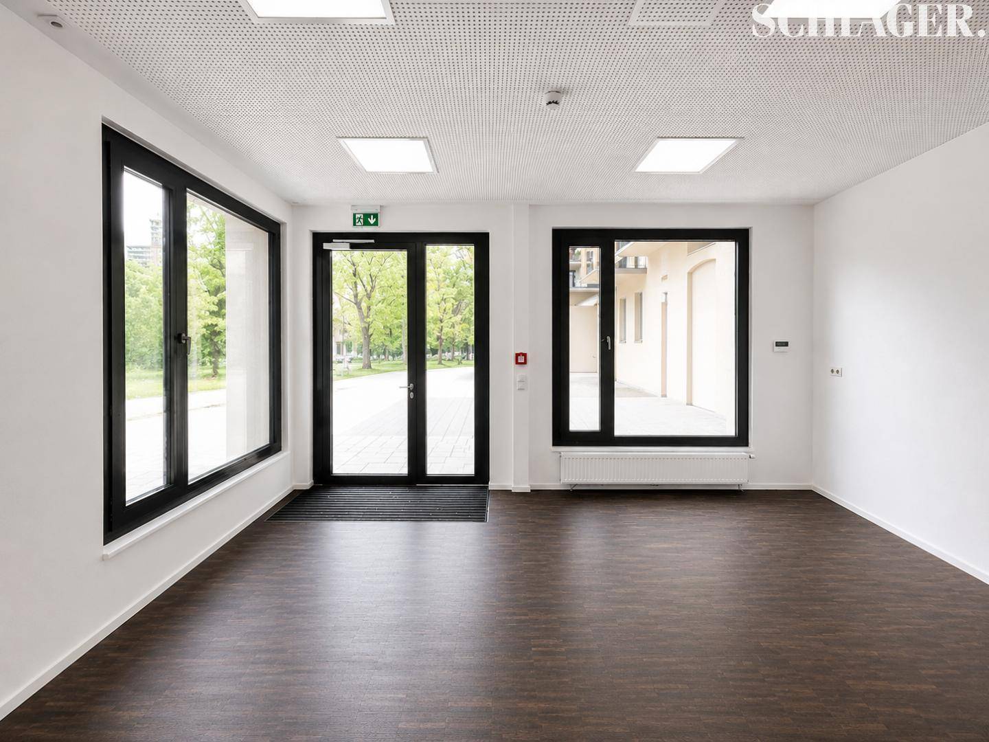 Geräumiger Eingangsbereich mit großen Glasfenstern und Doppeltür, die einen Blick ins Grüne freigibt.