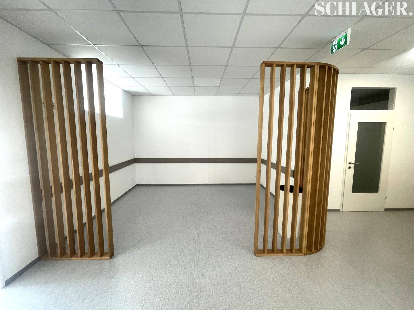 Geräumiger Empfangsbereich mit zwei dekorativen Holz-Raumteilern und hellem Vinylboden.