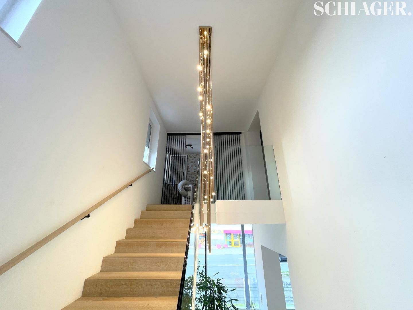 Moderne Holztreppe mit Glasgeländer und einer eleganten, vertikalen Beleuchtungsinstallation.