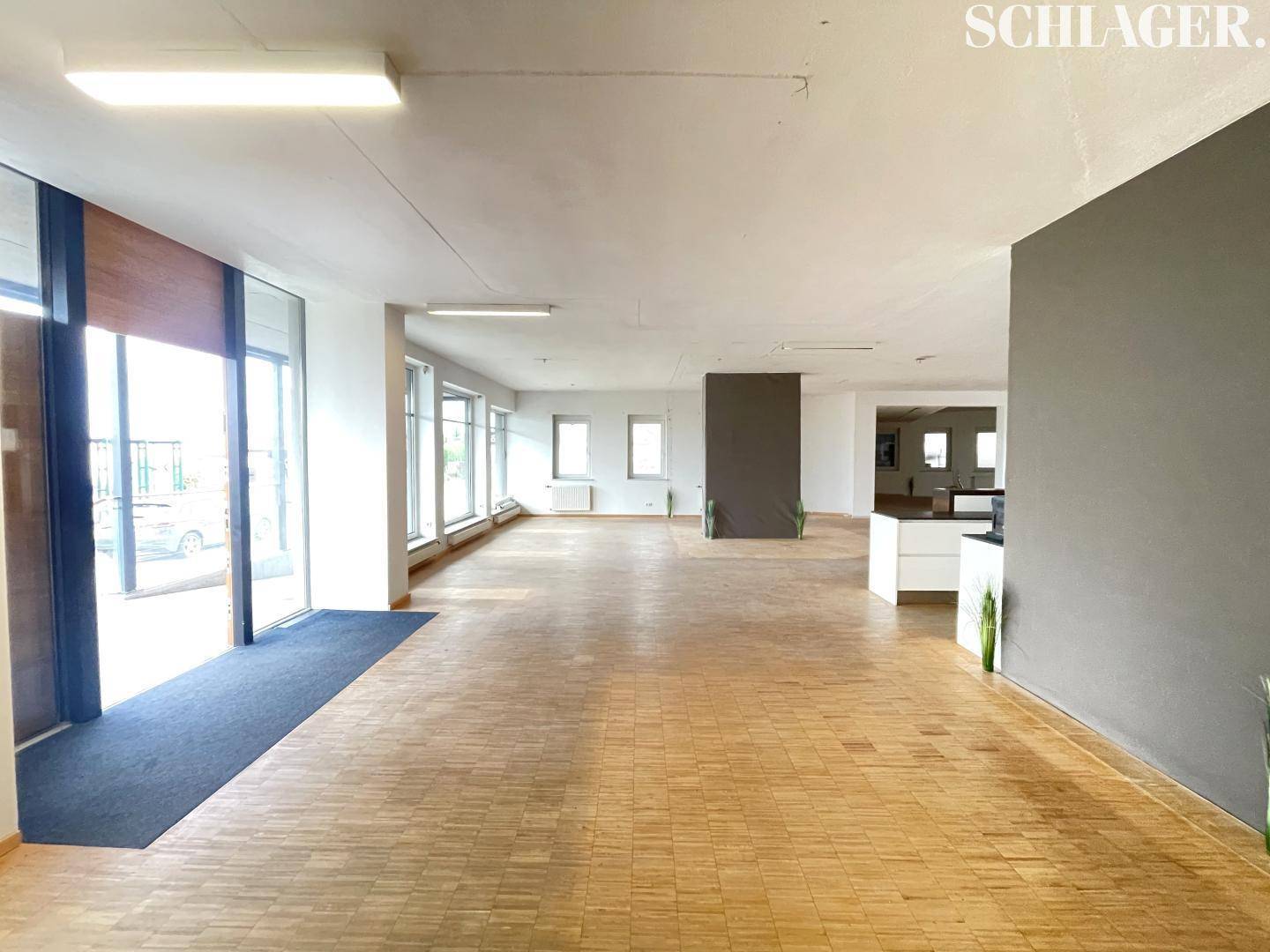 Weitläufiger Gewerberaum mit Eingangsbereich, großen Fensterfronten und durchgehendem Holzboden.