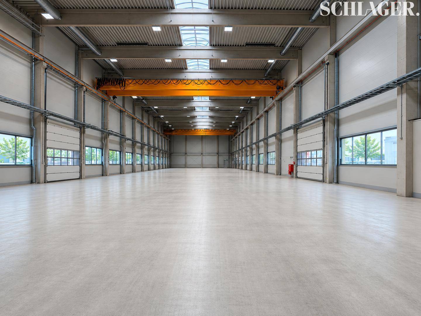 Geräumige, leere Lagerhalle mit hoher Decke, Oberlichtern und Krananlage.