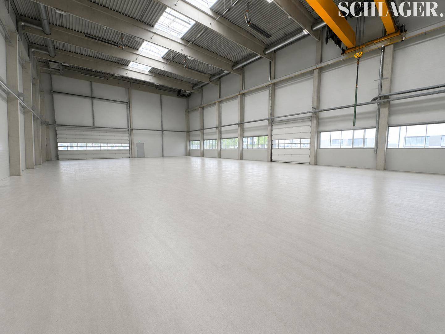 Weite Lagerhalle mit hohen Decken, Rolltoren, Oberlichtern und einem Laufkran.