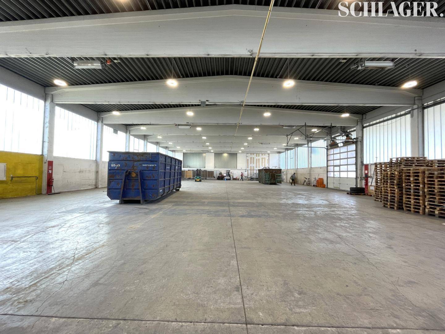 Weitläufige Lagerhalle mit Betonboden, hohen Decken und einem großen Abfallcontainer in der Mitte des Raumes.