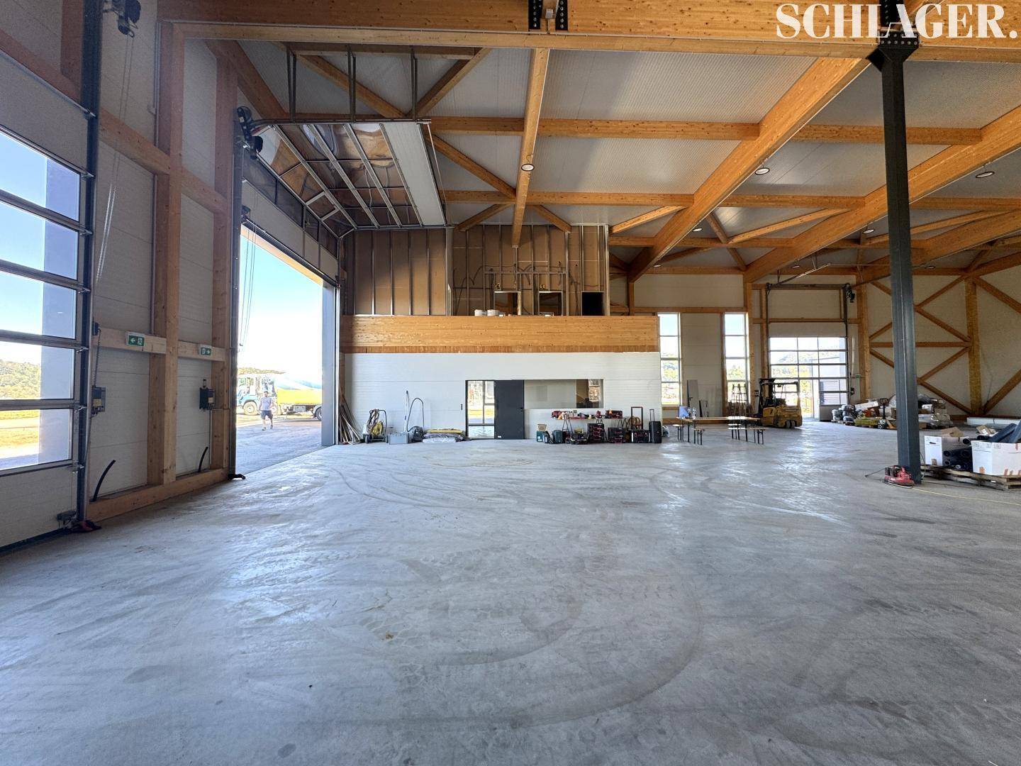 Helle Lagerhalle mit geöffnetem Rolltor, das den Blick nach draußen freigibt, und einer stabilen Holzkonstruktion.
