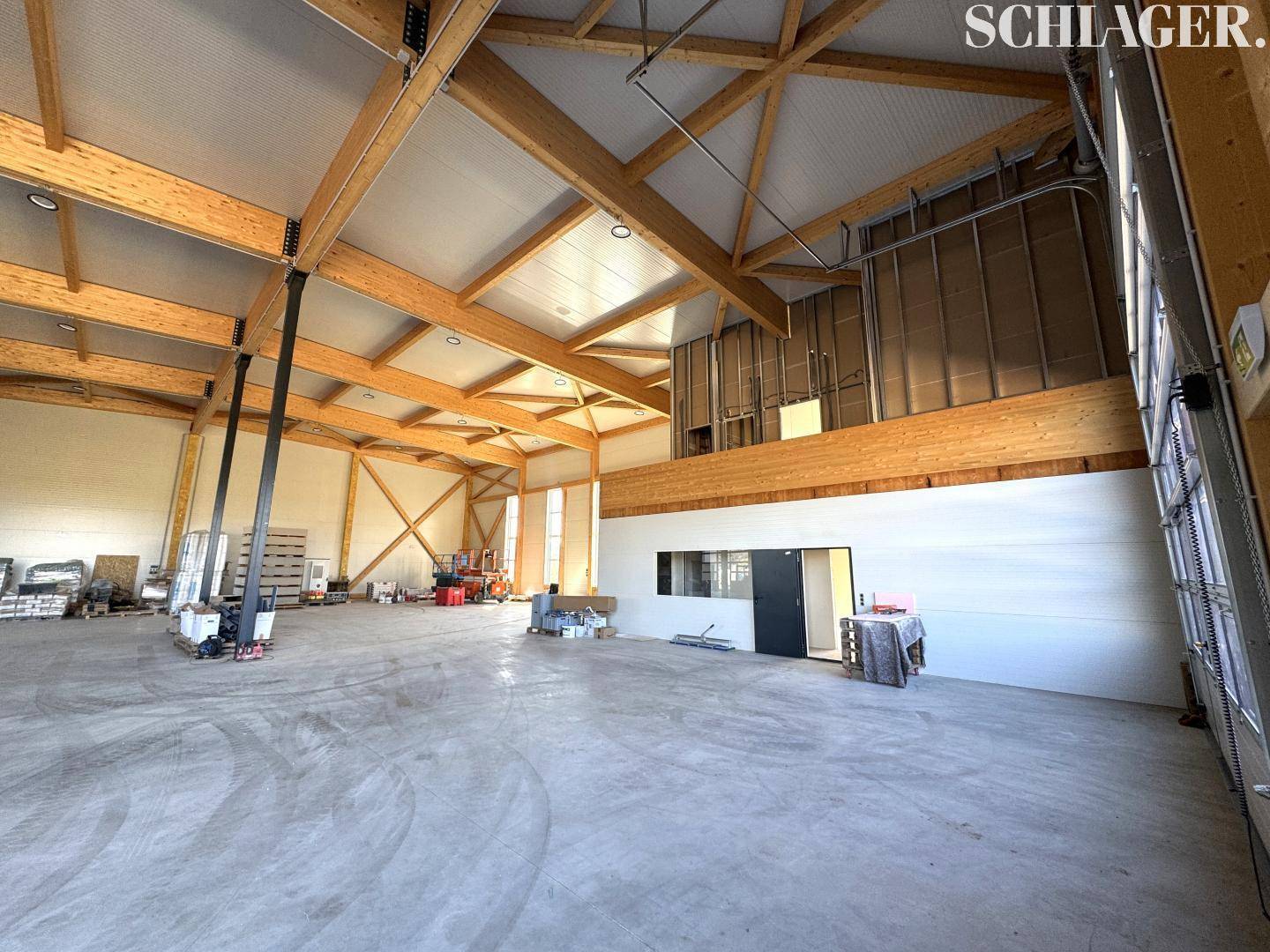 Geräumige Lagerhalle mit hohen Decken, sichtbaren Holzträgern und einem robusten Betonboden, hell beleuchtet.