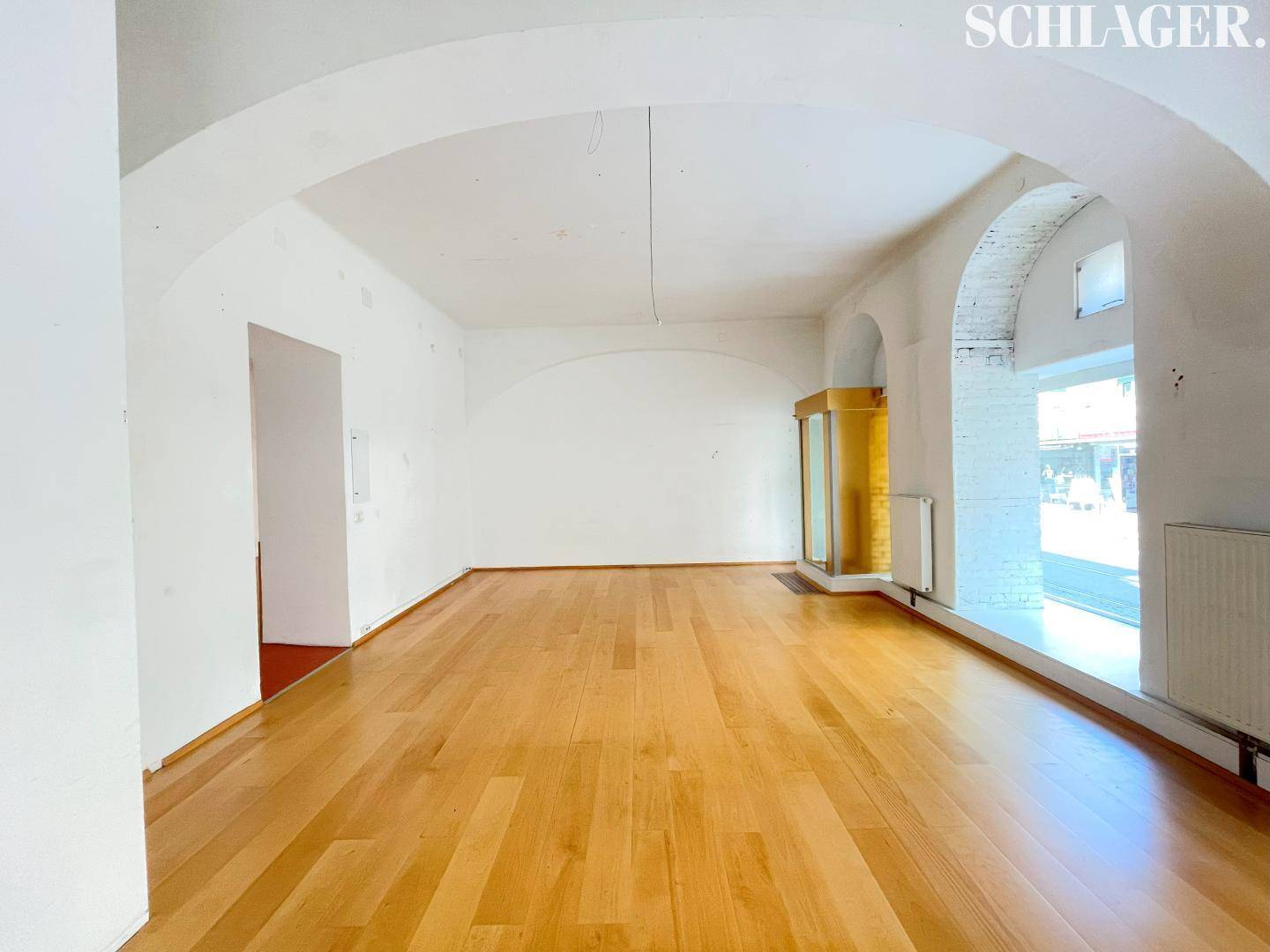 Geräumiger Innenraum mit Holzboden, weißen Wänden und einem dekorativen Bogen, viel Tageslicht durch Fenster.