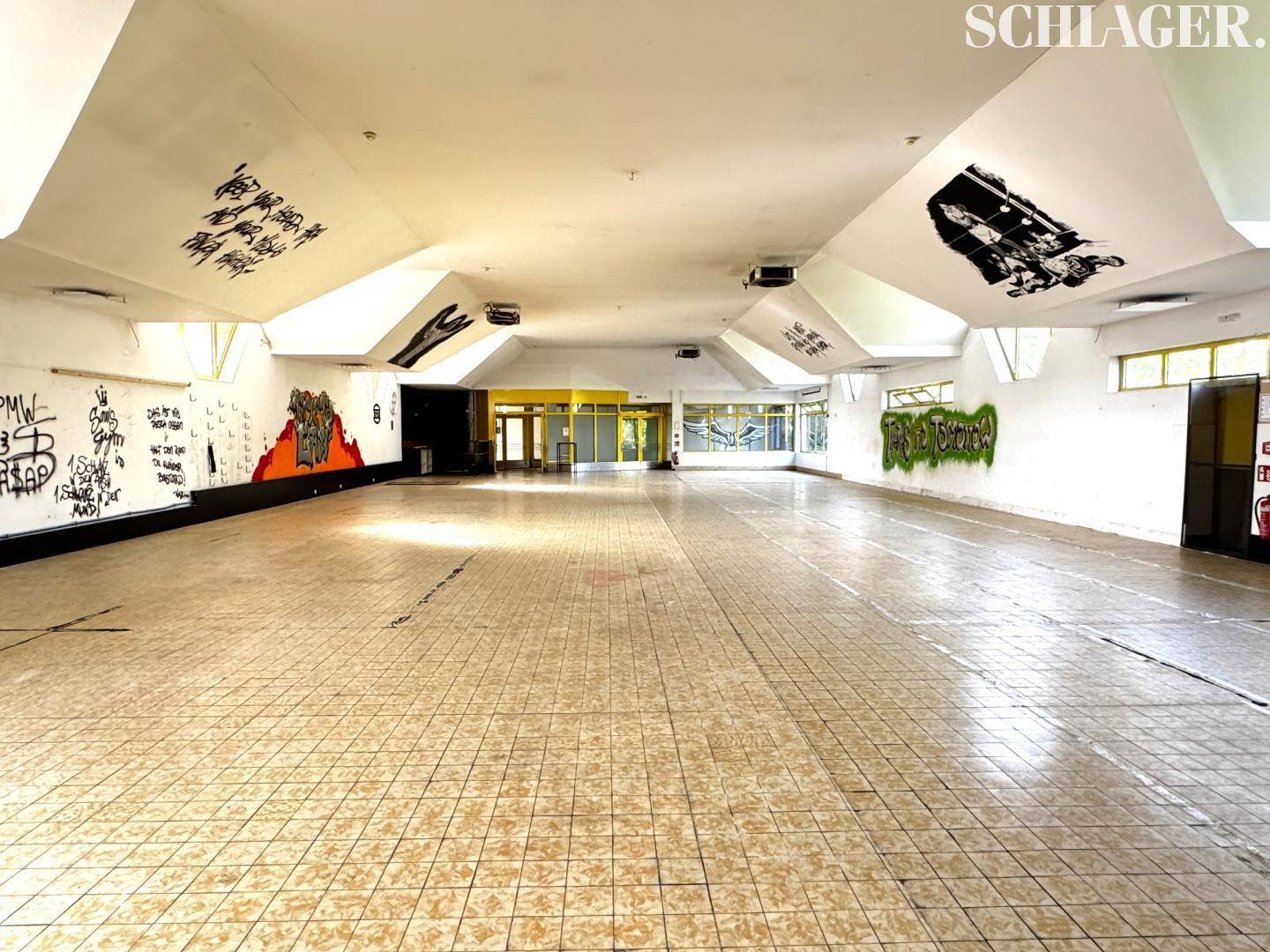 Großer, leerer Innenraum mit Fliesenboden, hohen Decken und Graffiti an Wänden und Decke.