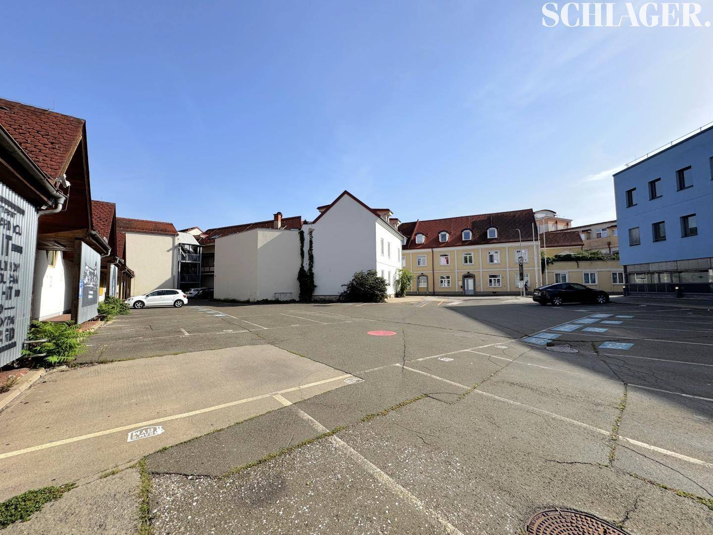 Großer Außenparkplatz umgeben von verschiedenen Gebäuden unter einem klaren blauen Himmel.