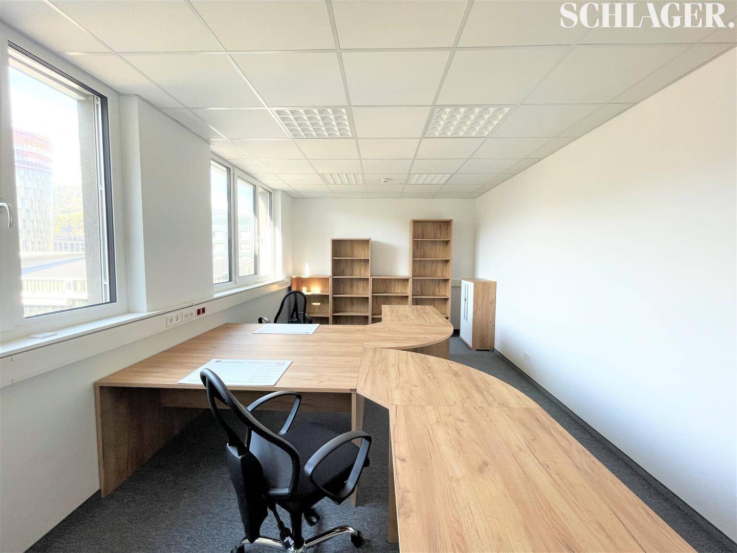 Helles Büro mit großem L-förmigem Schreibtisch, Bürostuhl und Regalen, mit Ausblick.
