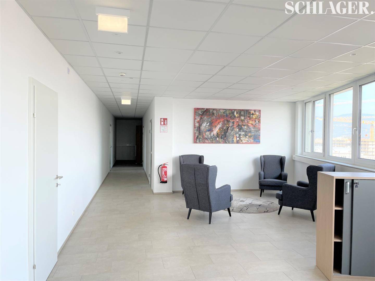 Gemütlicher Wartebereich mit Sesseln, Kunst an der Wand und großen Fenstern.