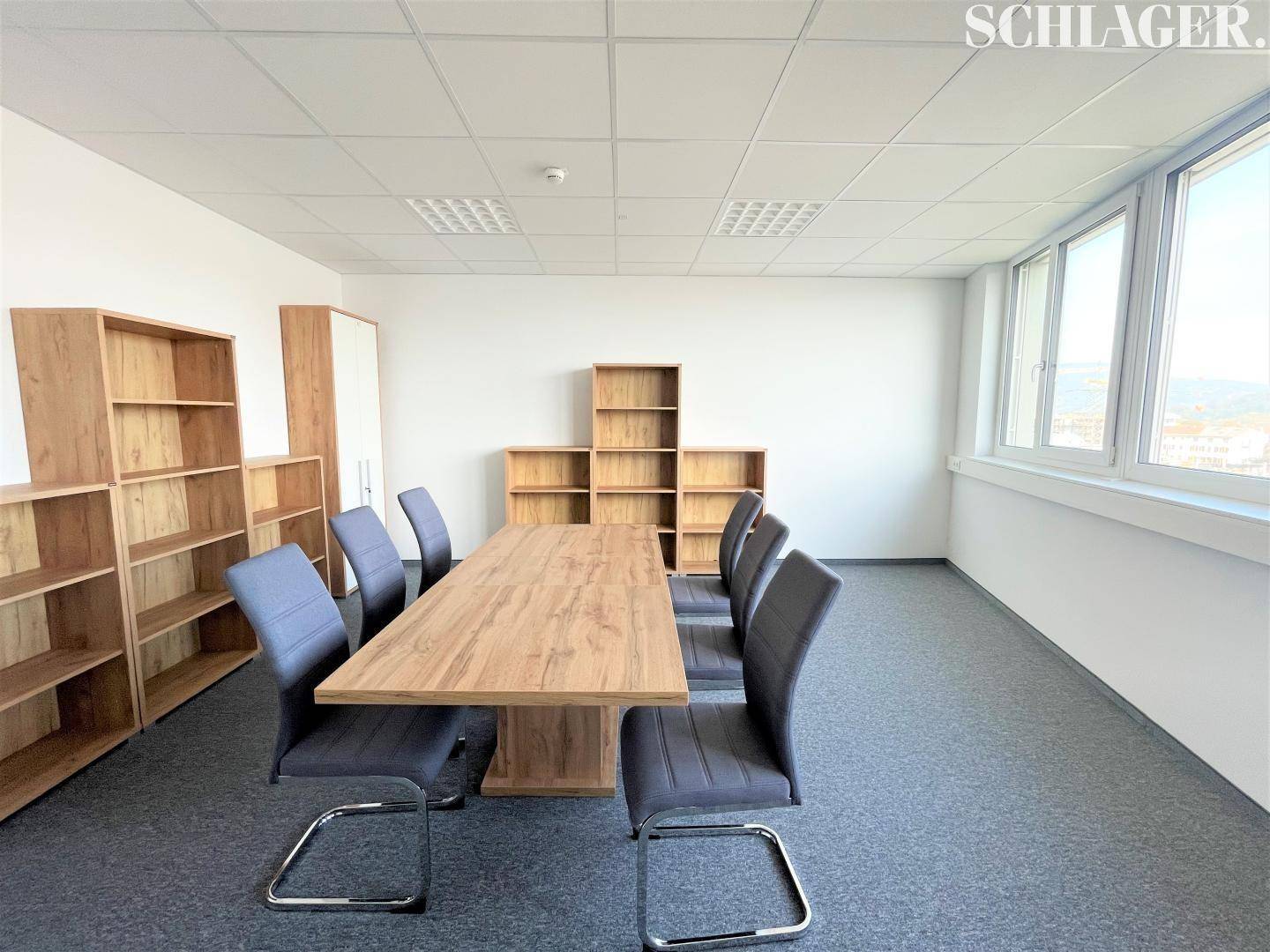 Großer Konferenzraum mit Holztisch, Bürostühlen und Regalen, viel Tageslicht.