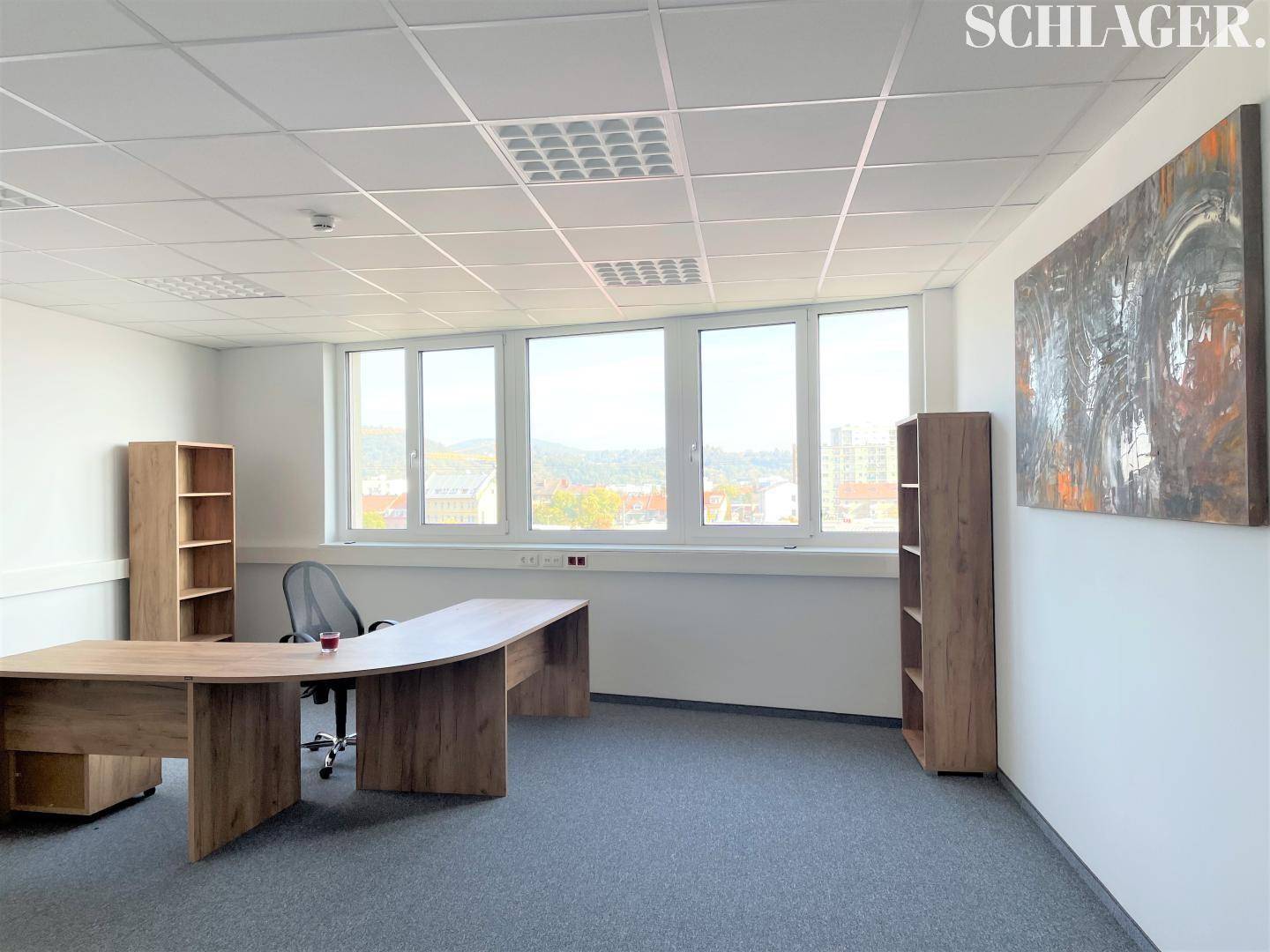 Modernes Büro mit geschwungenem Schreibtisch, Regalen und großen Fenstern mit Weitblick.