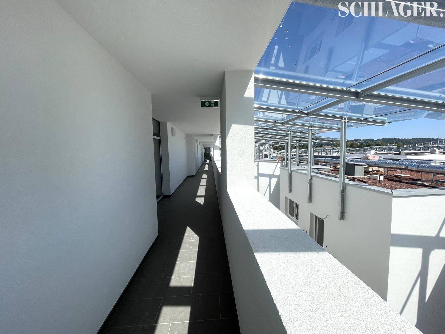Heller Flur in einem modernen Gebäude mit Glasdach und Blick auf die Umgebung.