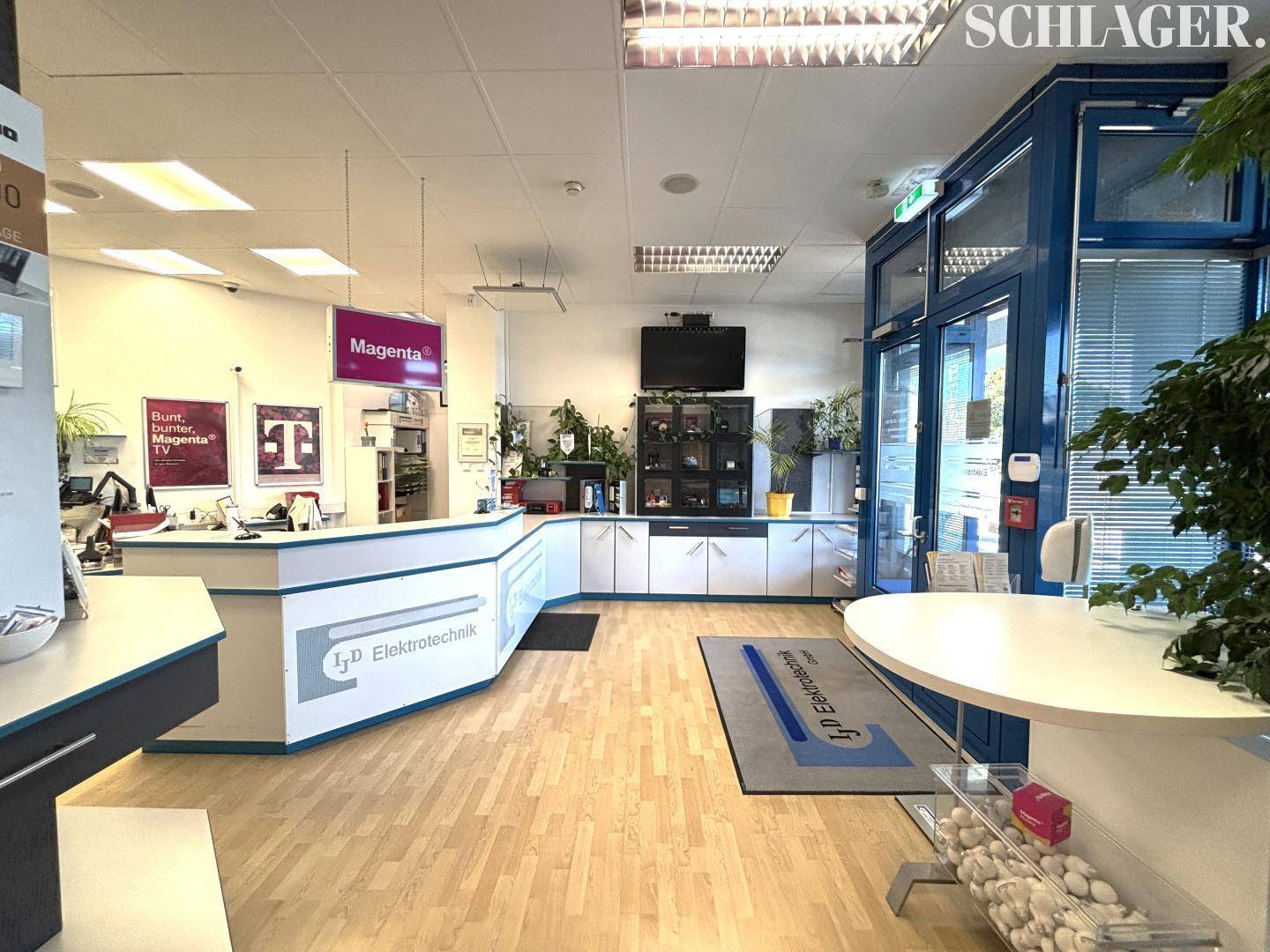 Heller Empfangsbereich oder Verkaufsraum mit einer Theke, Auslagen und einer Glasfront zum Eingang.